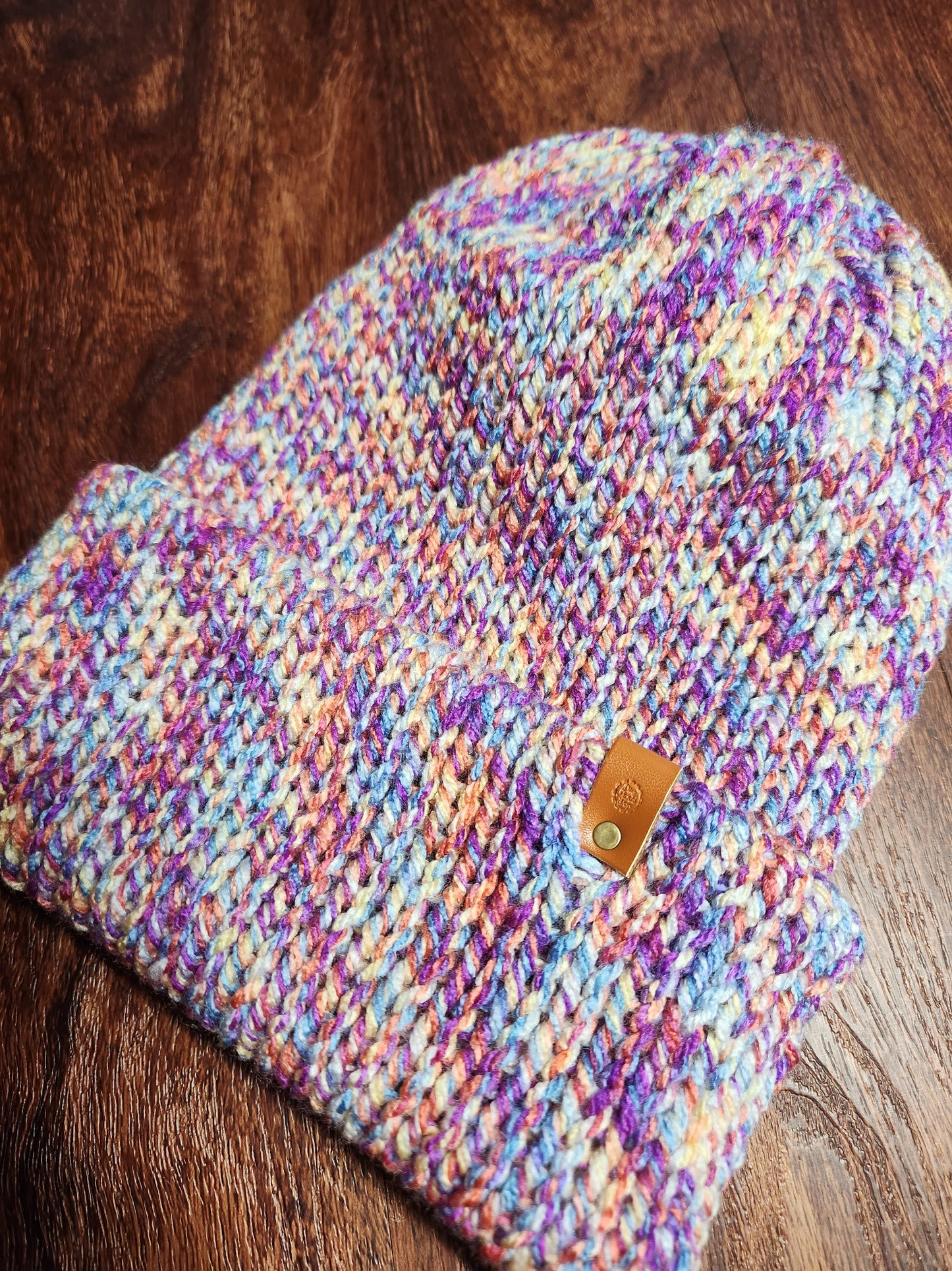 Multicolored knitted pouch with a leather patch on a wooden surface