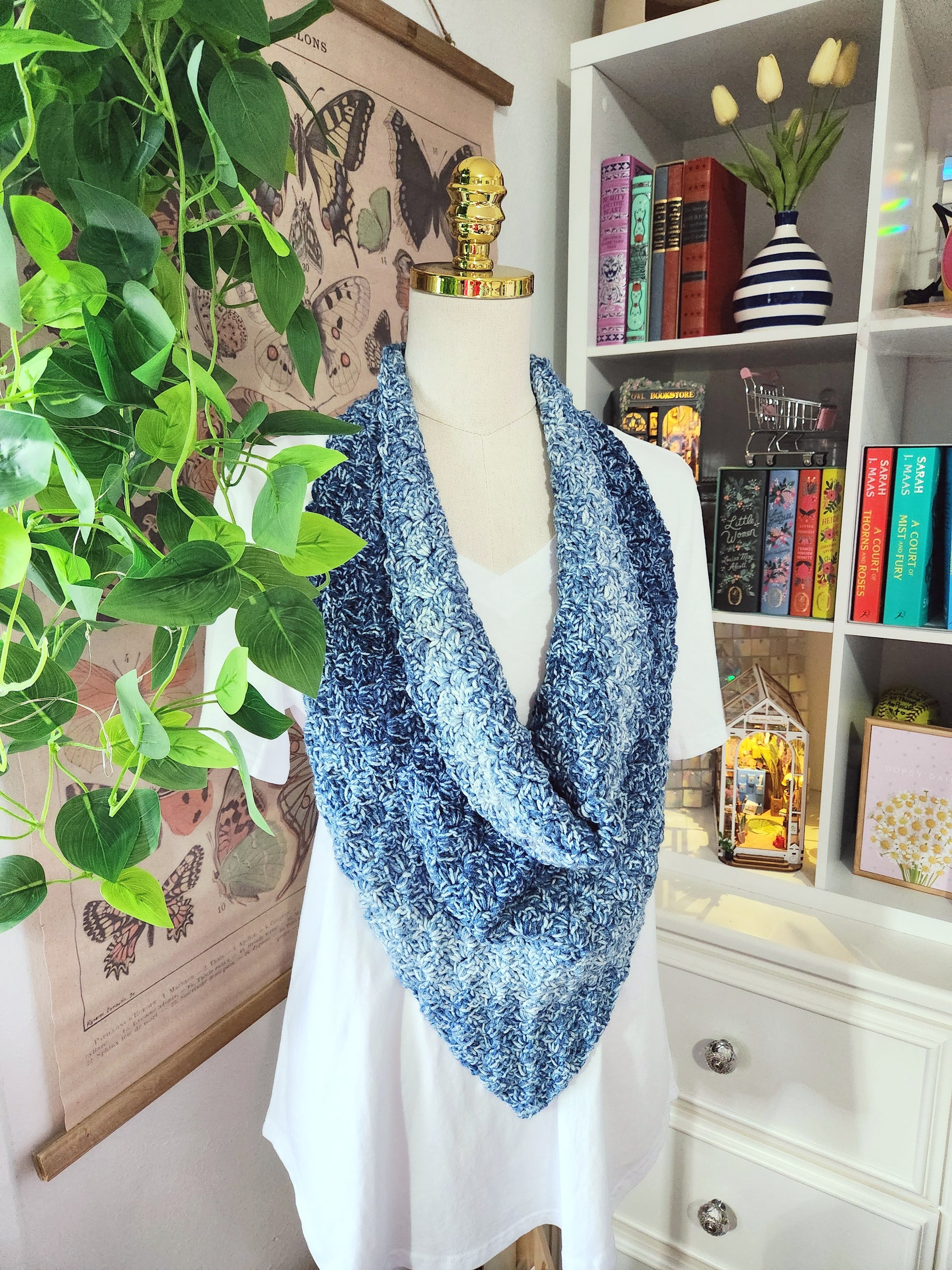 Mannequin wearing a blue patterned shawl in front of a bookshelf and plant