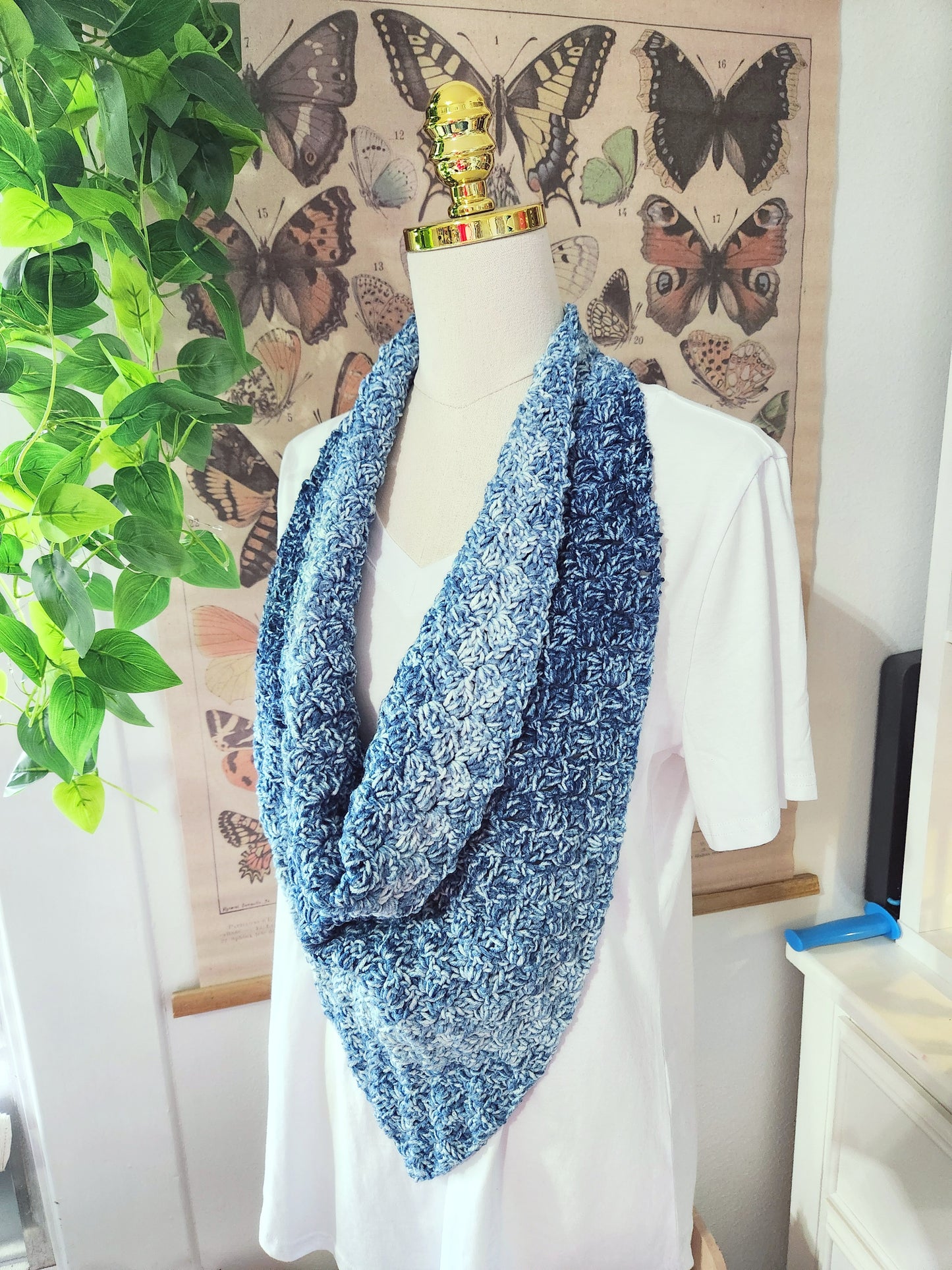Mannequin wearing a blue knitted scarf with butterfly artwork in the background