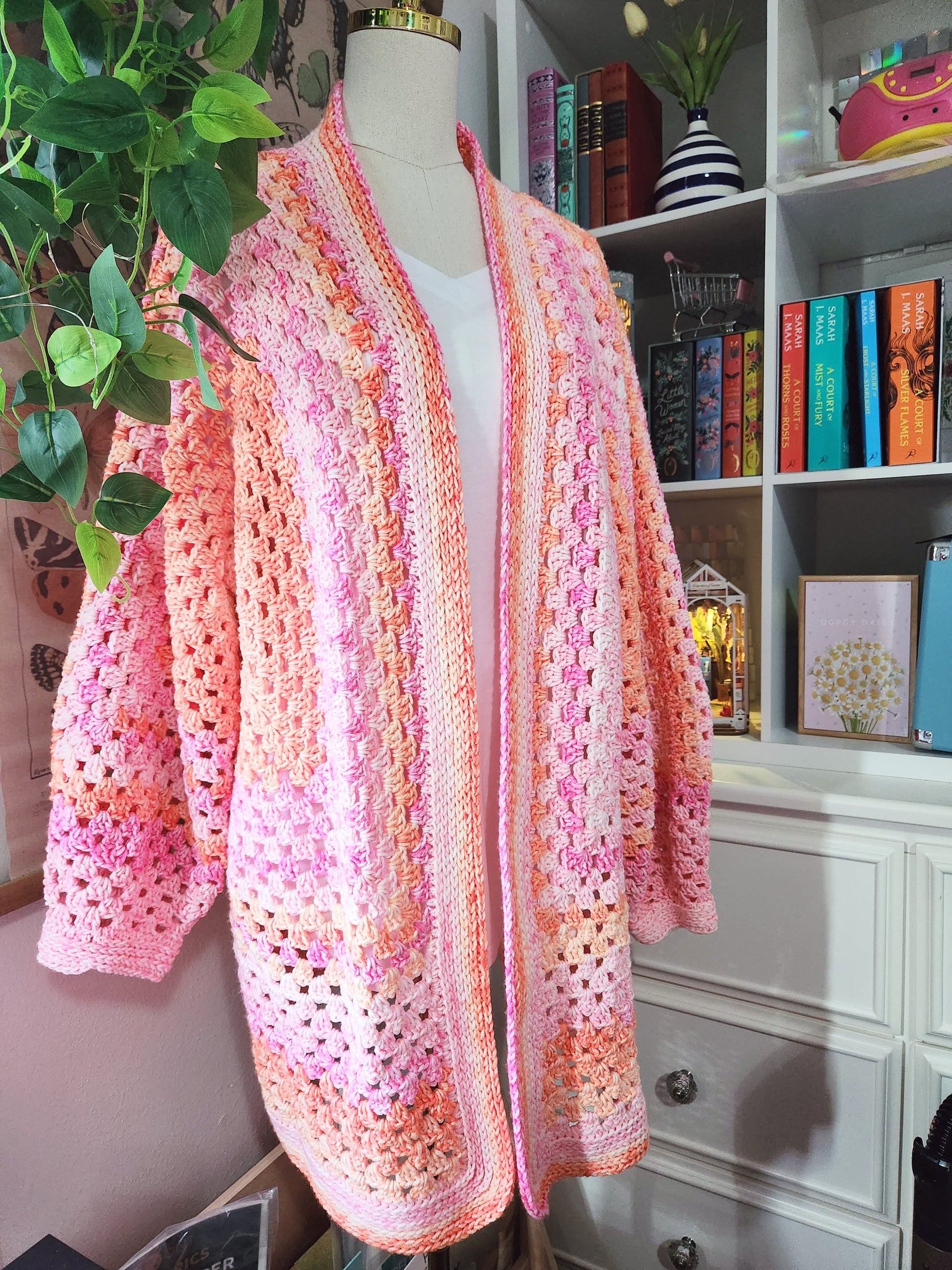 Crocheted cardigan on a mannequin in front of a bookshelf