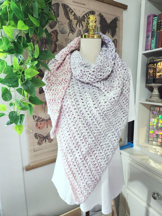 Mannequin wearing a pink knitted shawl in a room with plants and books.