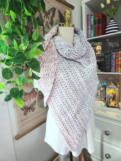 Mannequin wearing a pink and white patterned shawl in a room with books and plants.