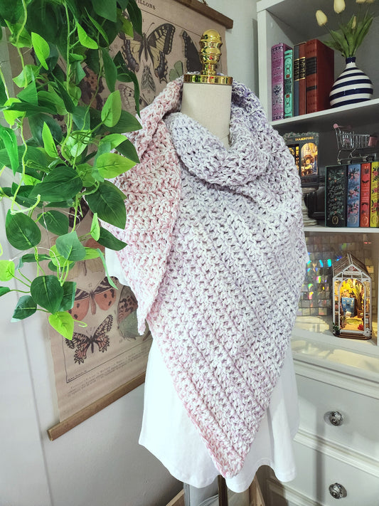 Mannequin wearing a pink and white patterned shawl in a room with books and plants.