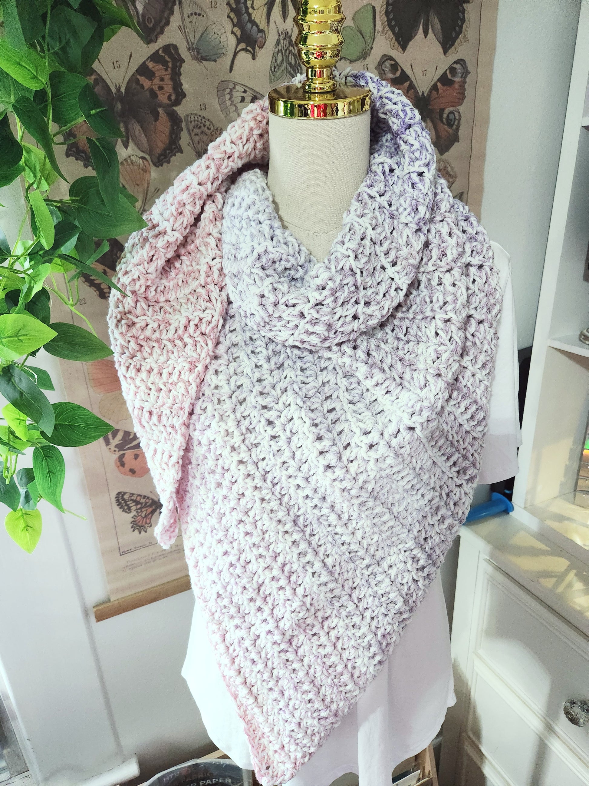 Mannequin wearing a pink and white crocheted shawl with butterfly wallpaper in the background