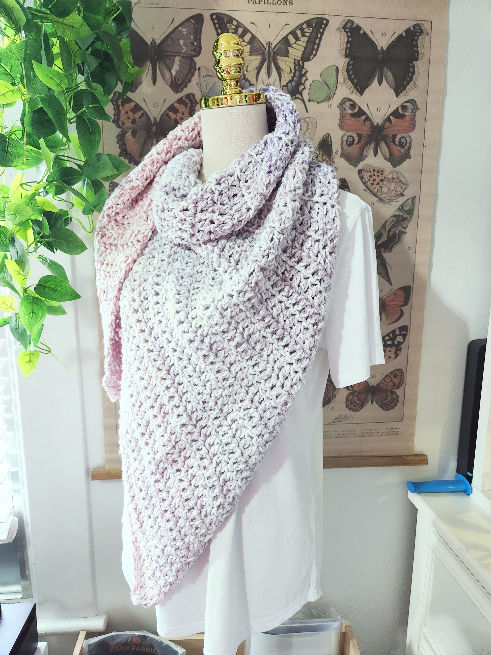 Mannequin wearing a pink crochet shawl with butterfly decorations in the background