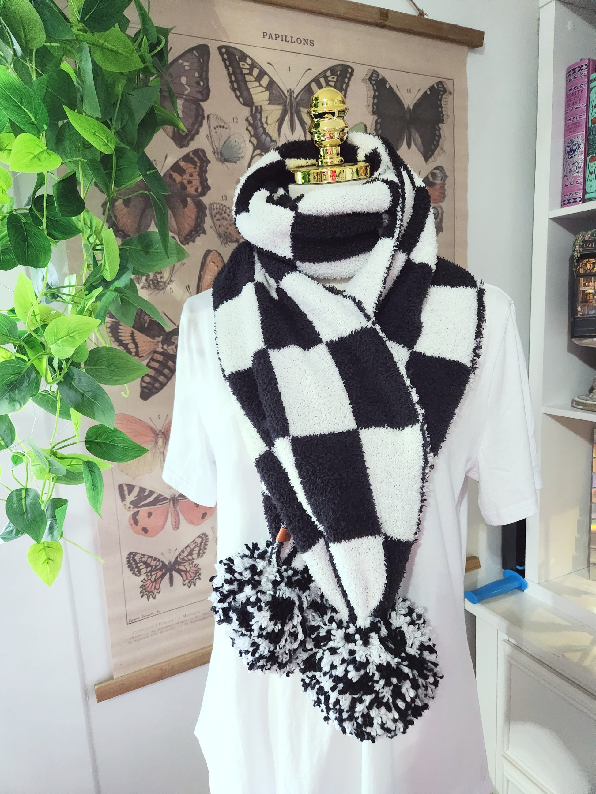 Person wearing a black and white checkered scarf with floral ends, standing in a room with butterfly decorations on the wall.