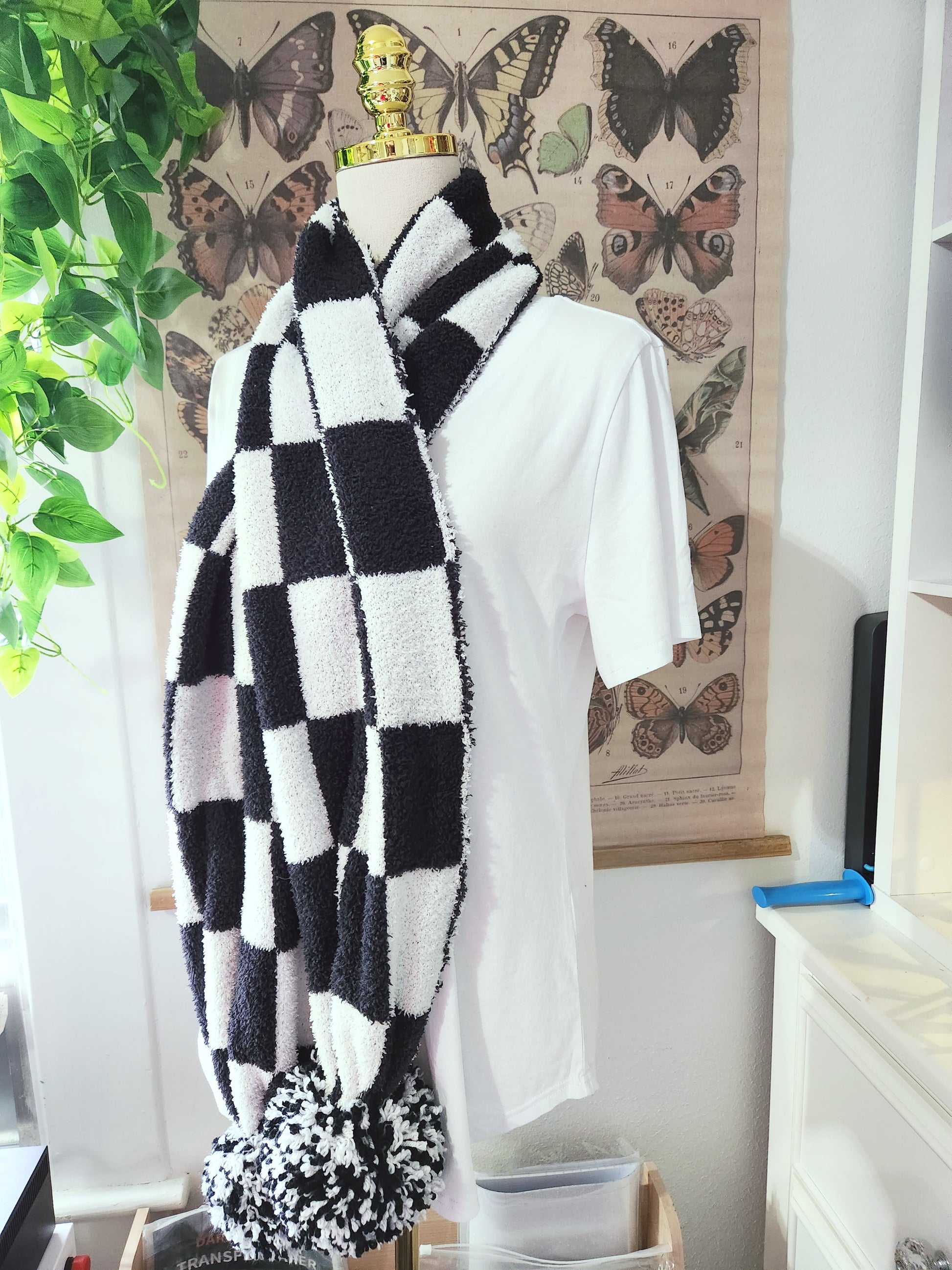 Mannequin wearing a black and white checkered scarf with butterfly poster in the background
