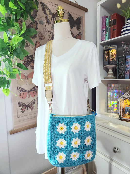 Mannequin wearing a white shirt with a blue crochet bag featuring white flowers, in a room with books and plants.