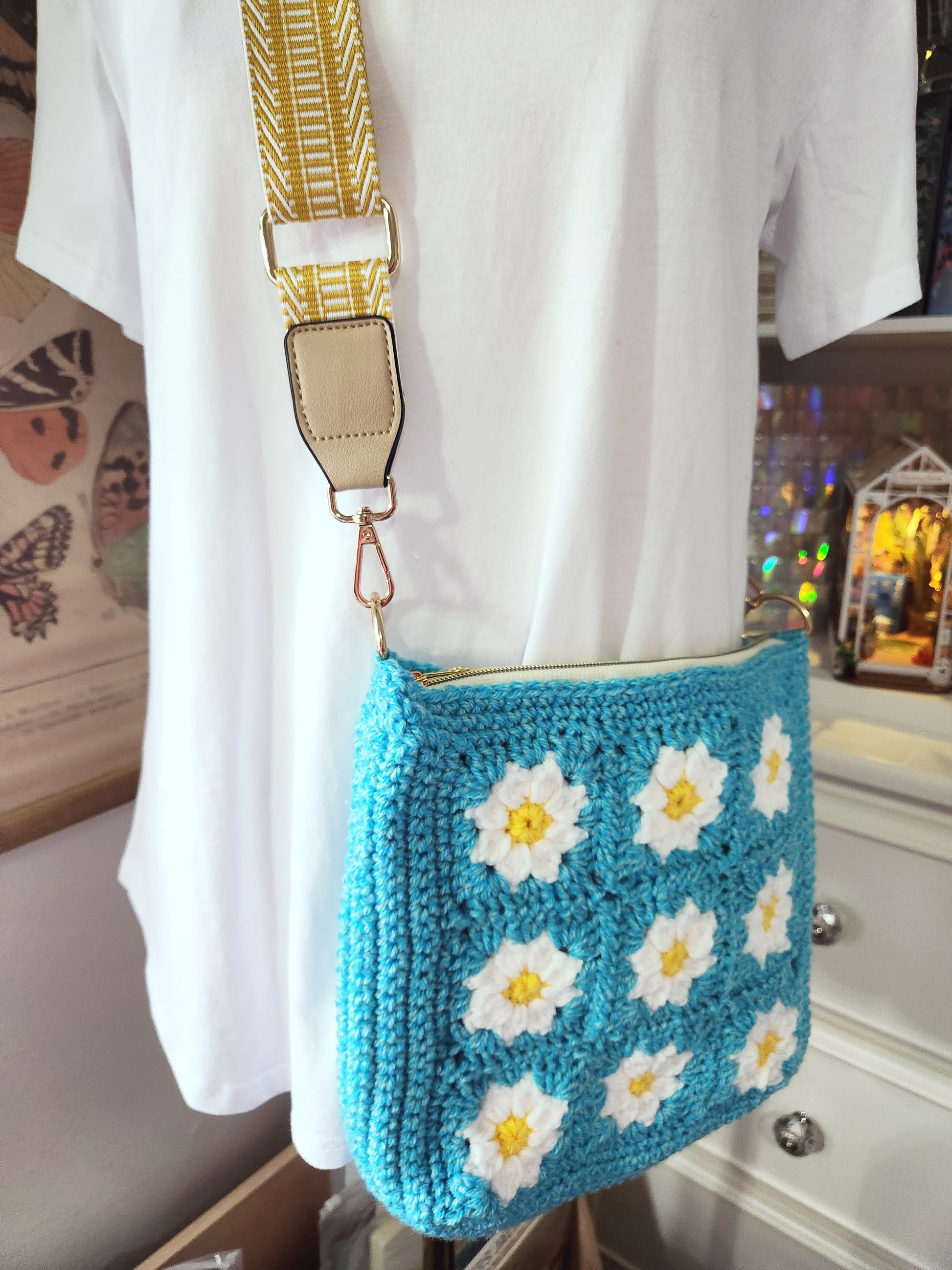 Blue crochet bag with white daisy patterns worn over a white shirt.