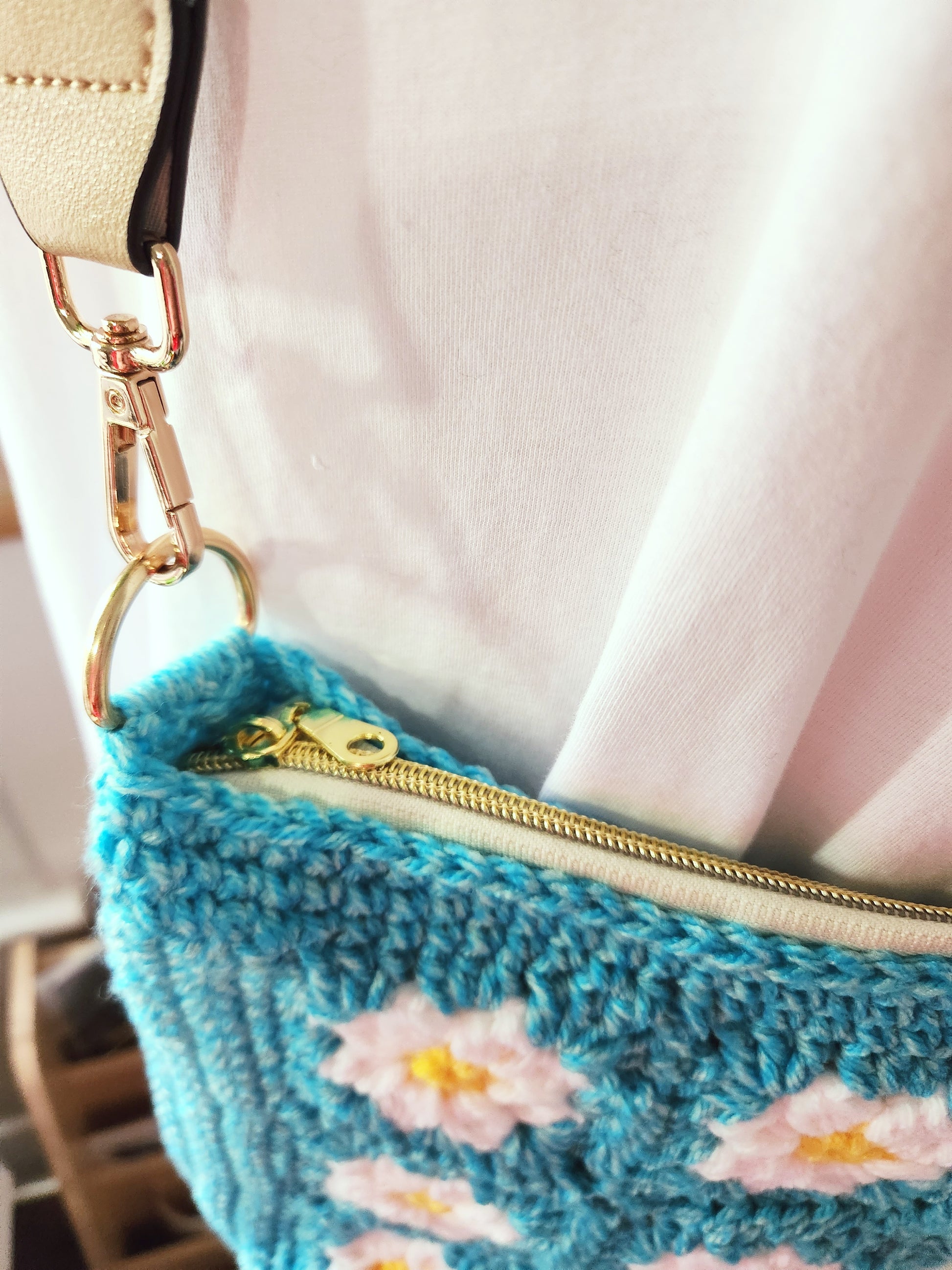 Blue knitted bag with floral patterns and a gold zipper, held by a person wearing a pink top.
