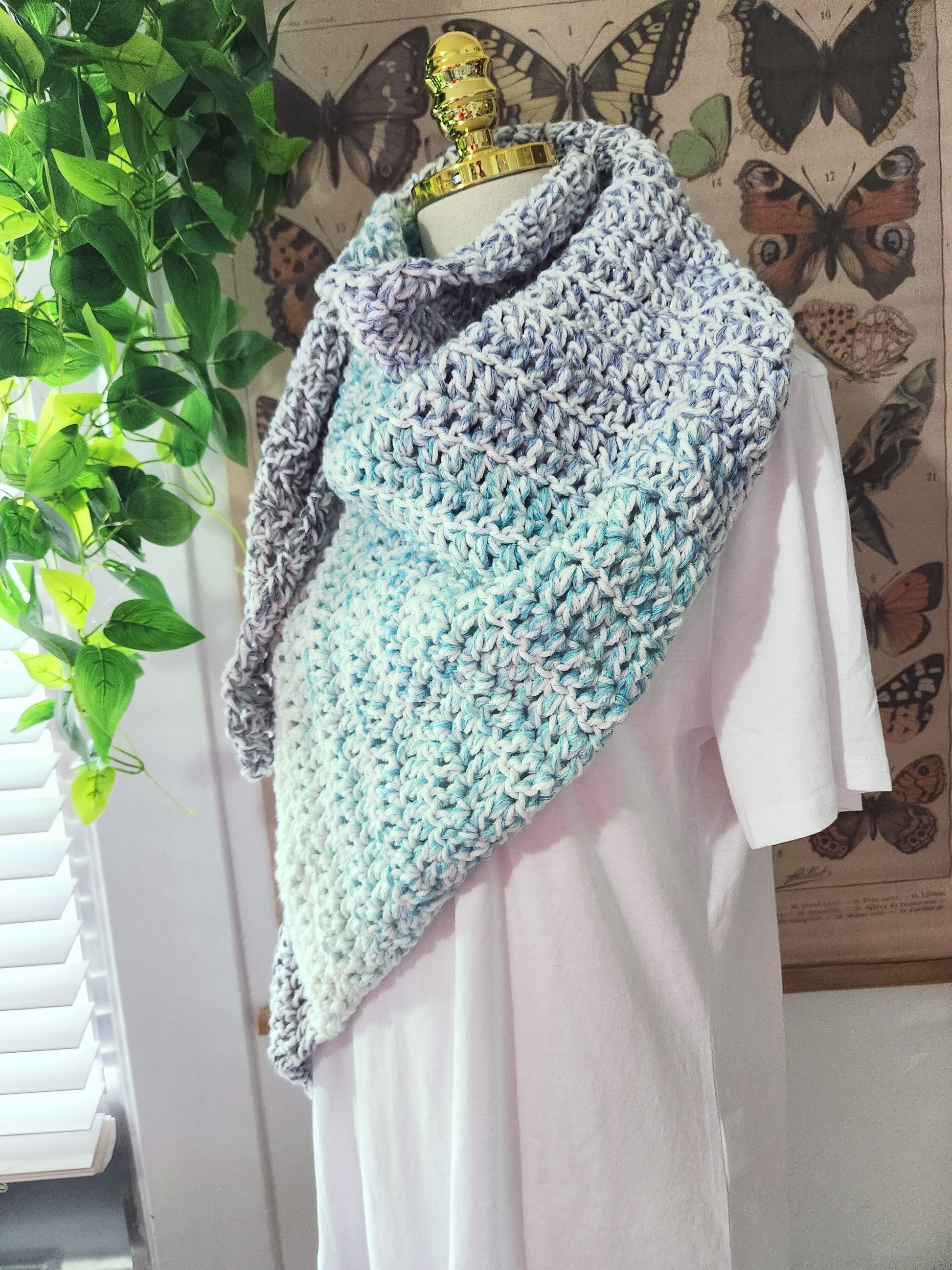 Knitted shawl draped over a mannequin against a butterfly-themed wall.