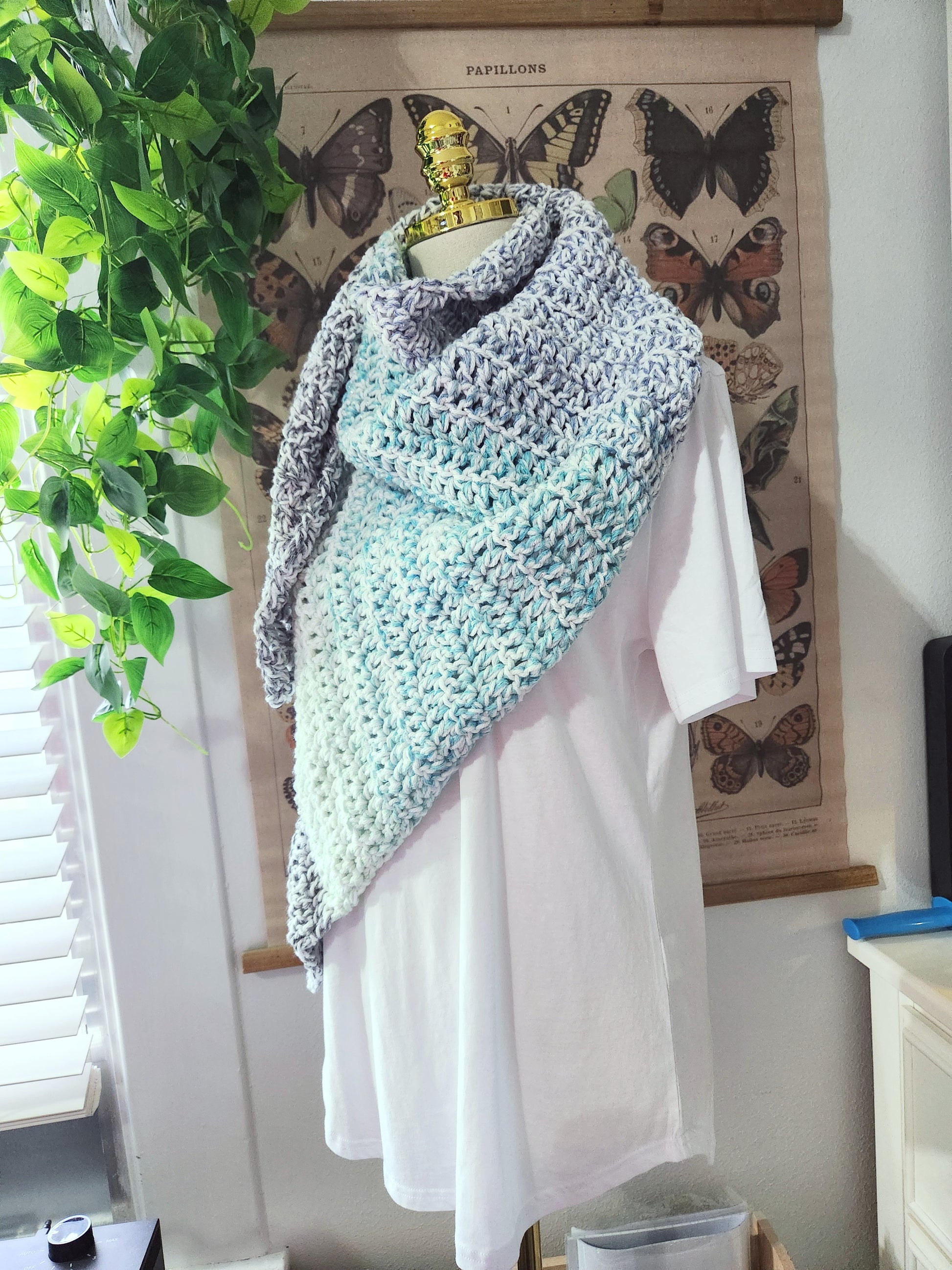 Mannequin wearing a crocheted shawl with butterfly poster in the background