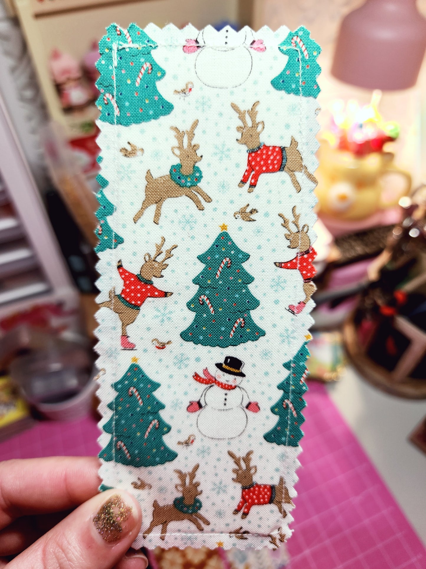 Christmas-themed fabric with reindeer and trees held by a hand against a blurred background