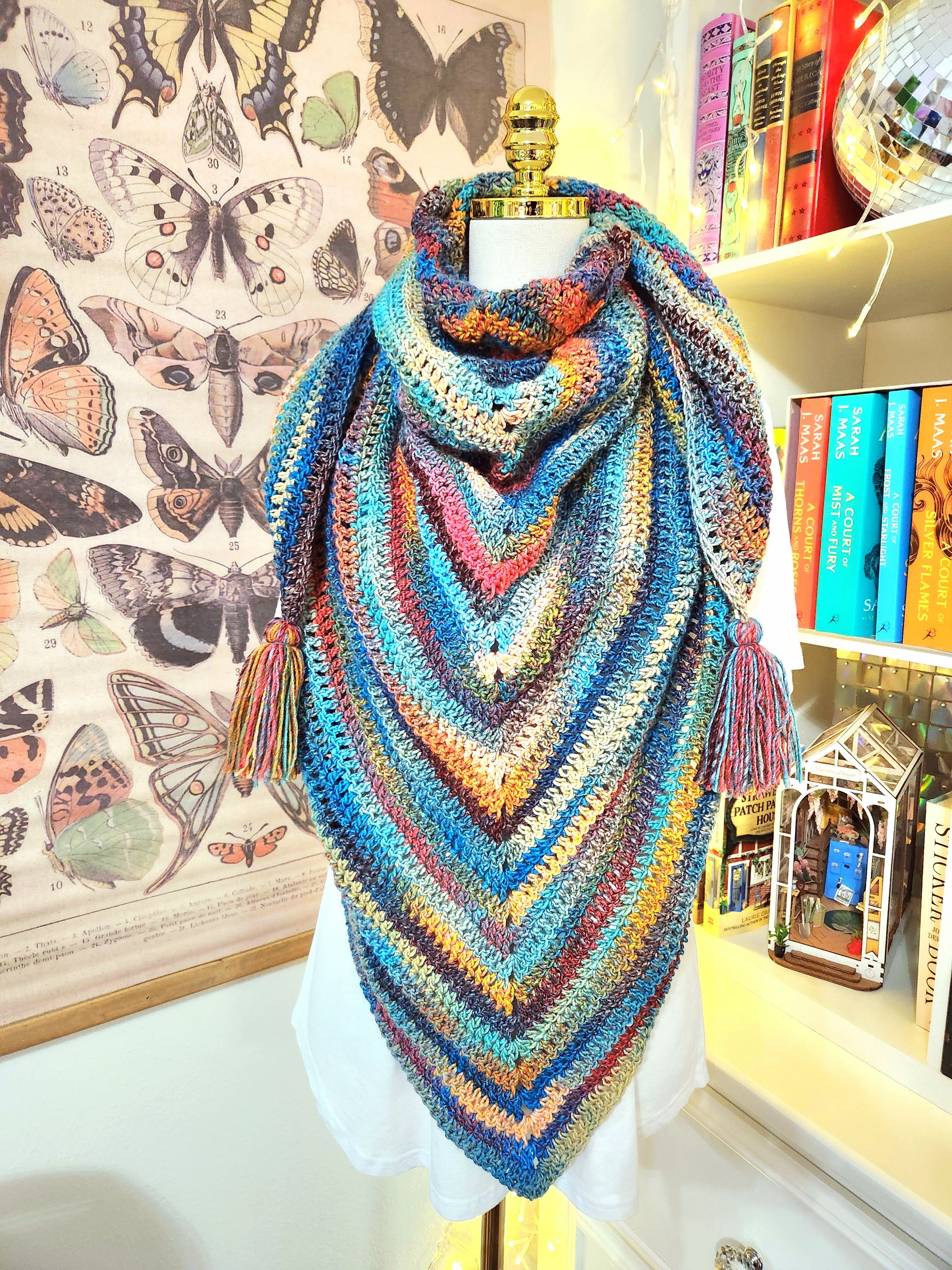 Colorful crocheted shawl on a mannequin with butterfly illustrations in the background