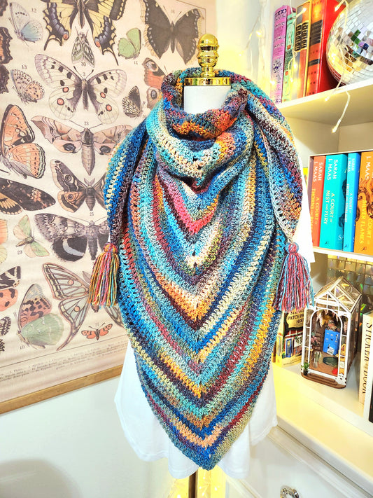 Colorful crocheted shawl on a mannequin with butterfly illustrations in the background