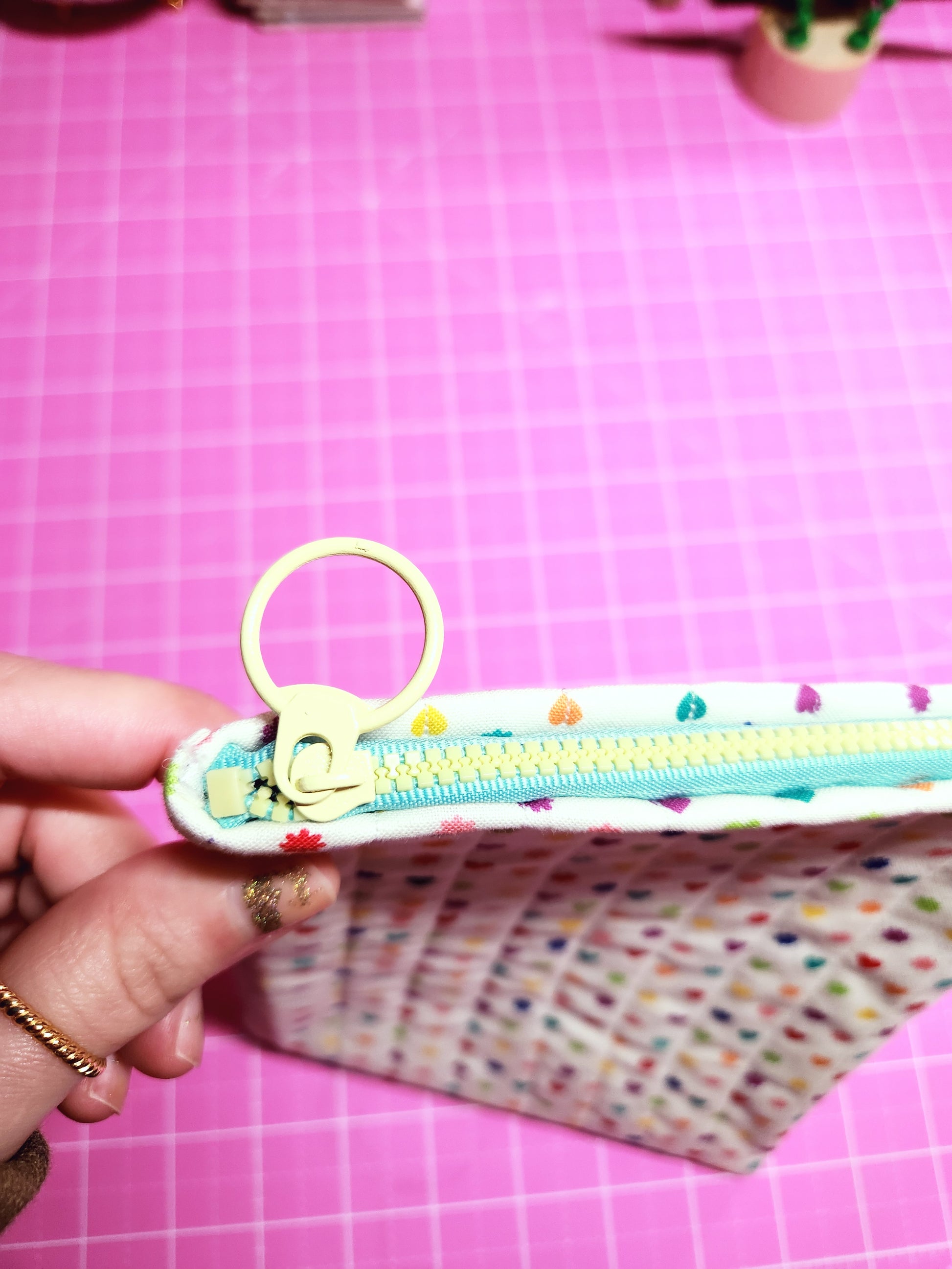 Hand holding a colorful keychain with a pink grid background