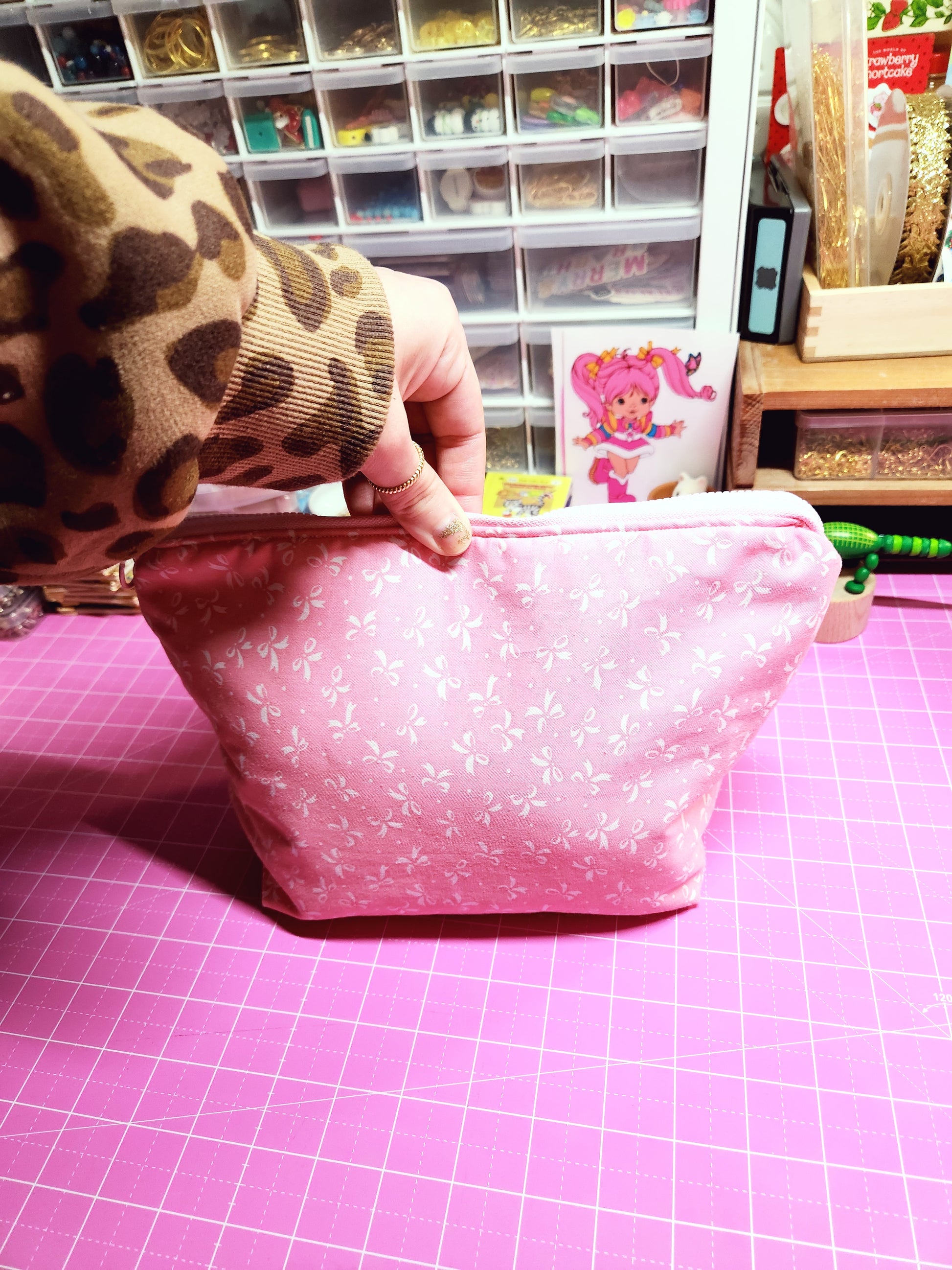 Pink fabric with white polka dots held by a hand against a pink grid background