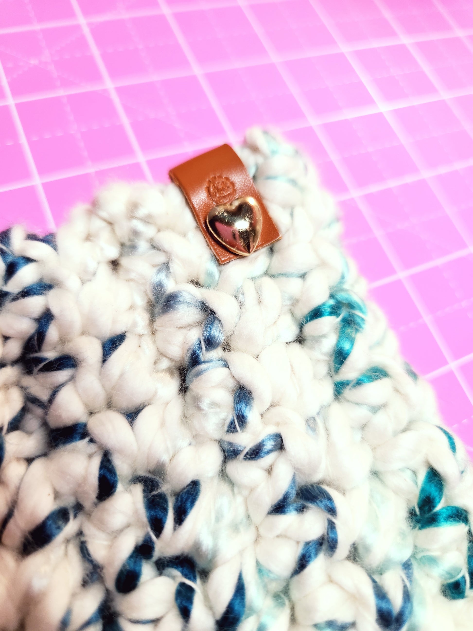 Close-up of a knitted item with a brown leather patch on a pink grid background