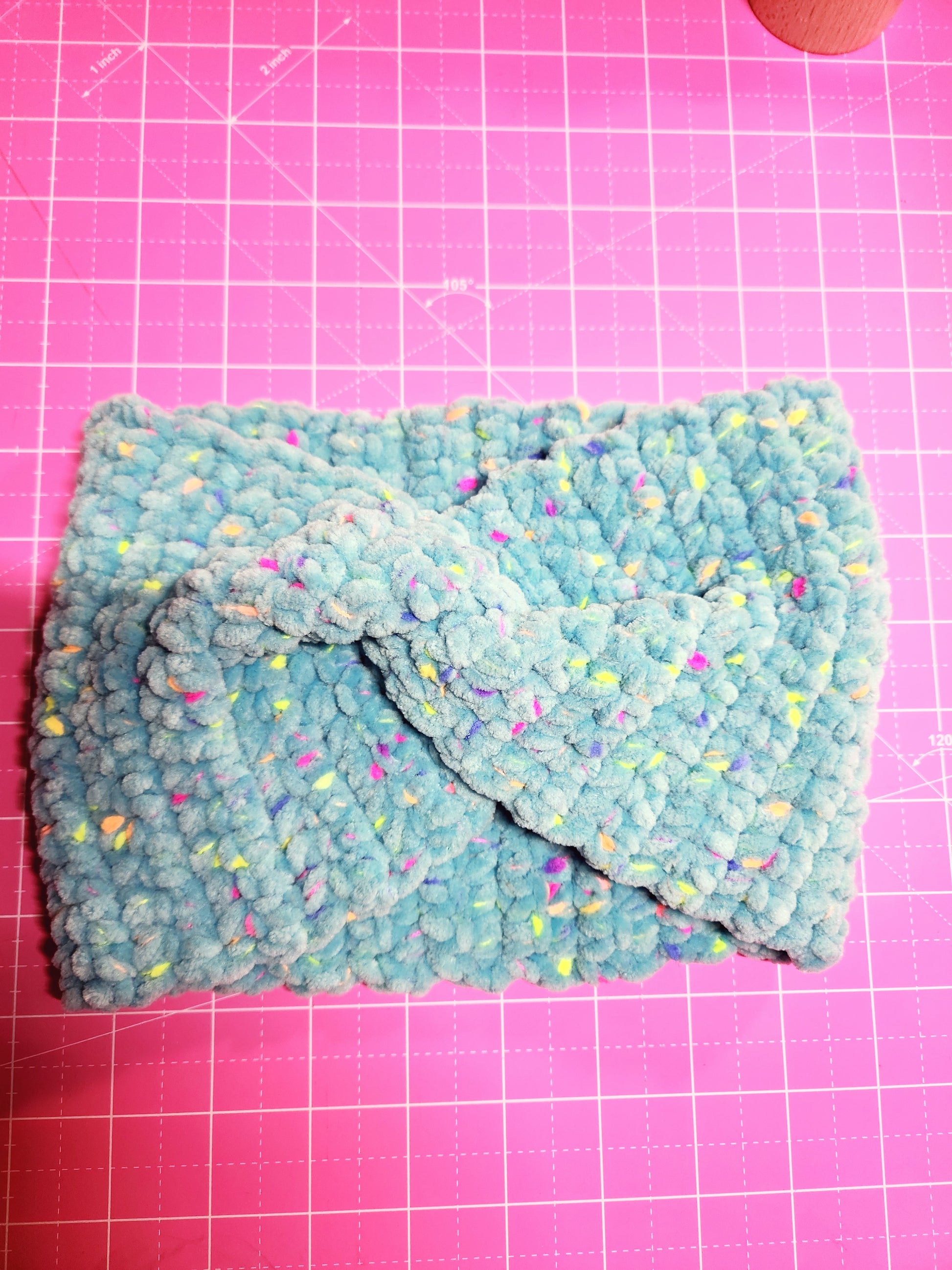 Folded blue fabric with colorful specks on a pink grid background