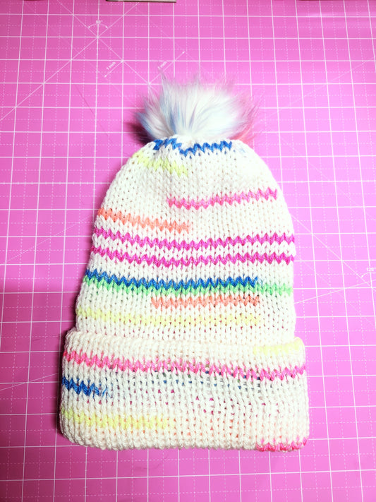 Colorful striped knit hat with a pom-pom on a pink grid background