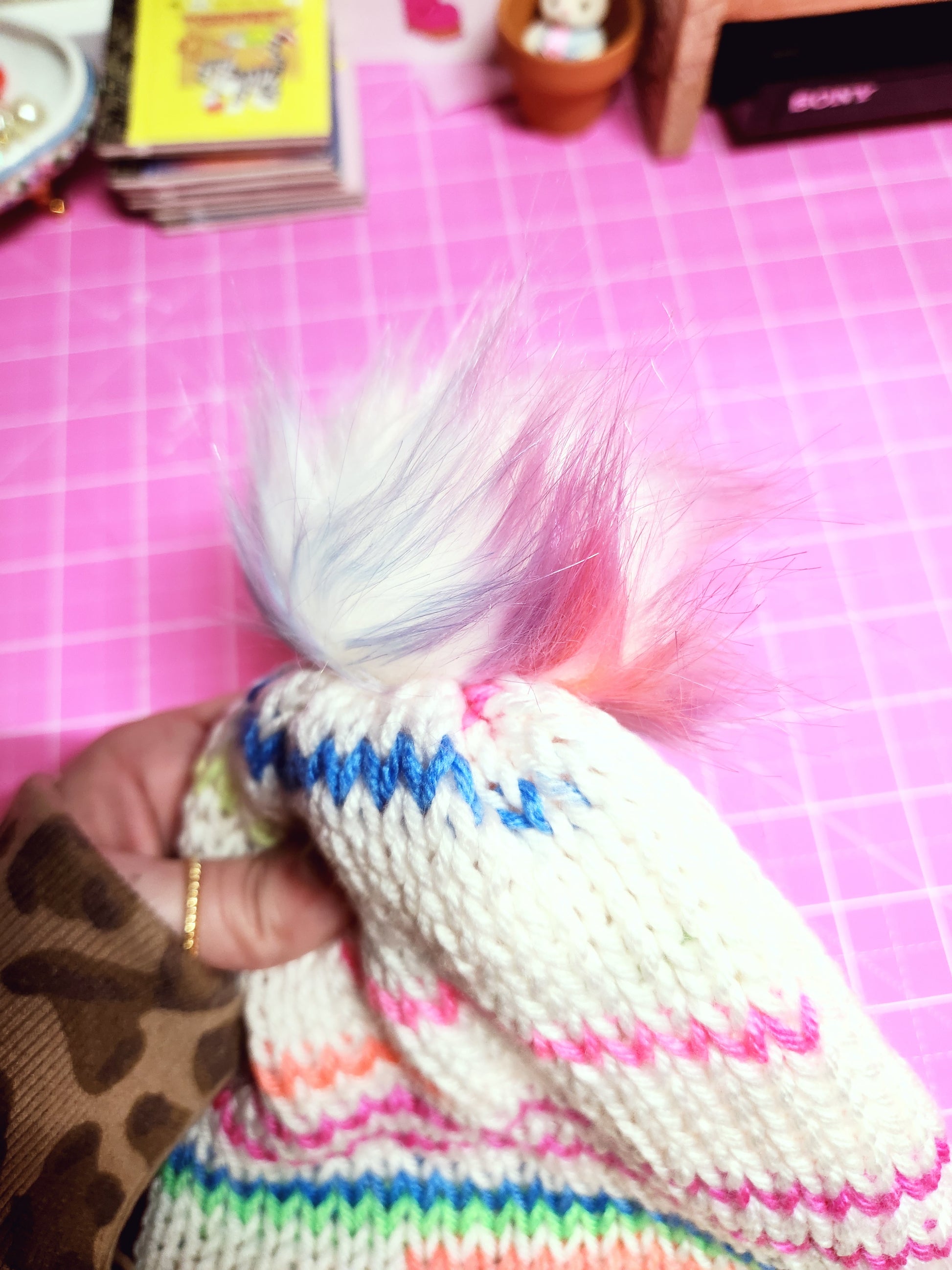 Colorful knitted item held by a hand on a pink grid background