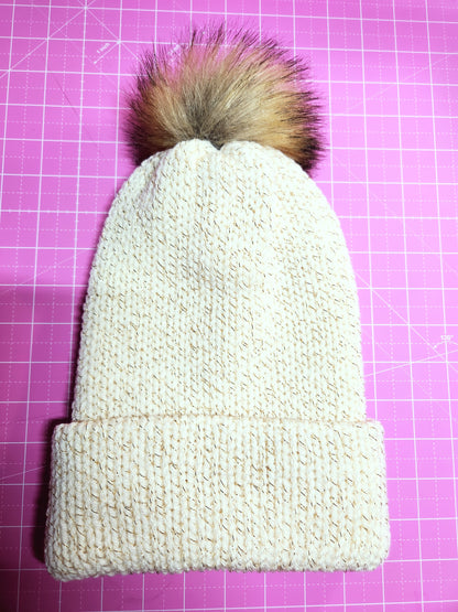 Knitted beanie with a fur pom-pom on a pink grid background
