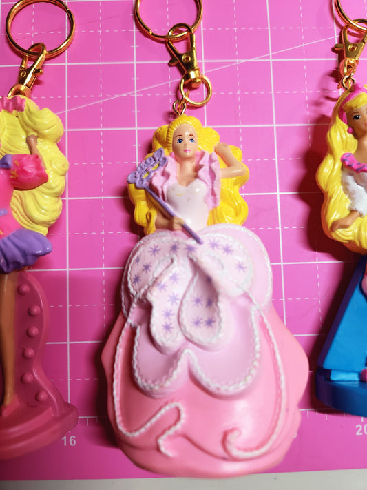 Keychains with fairy and princess designs on a pink surface