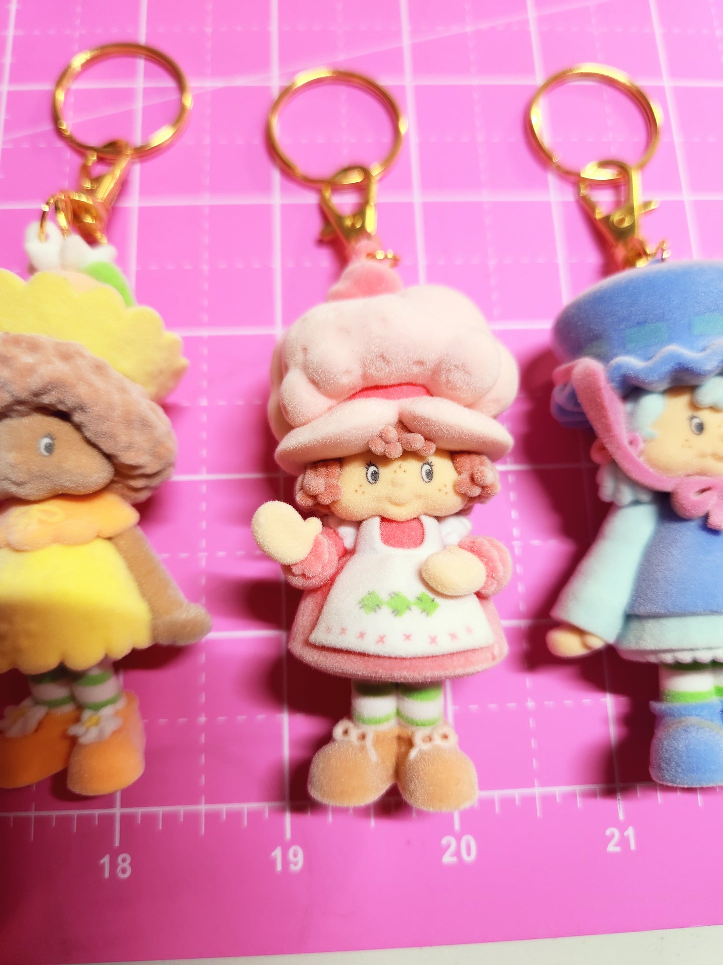 Colorful keychains shaped like cartoon characters on a pink grid background