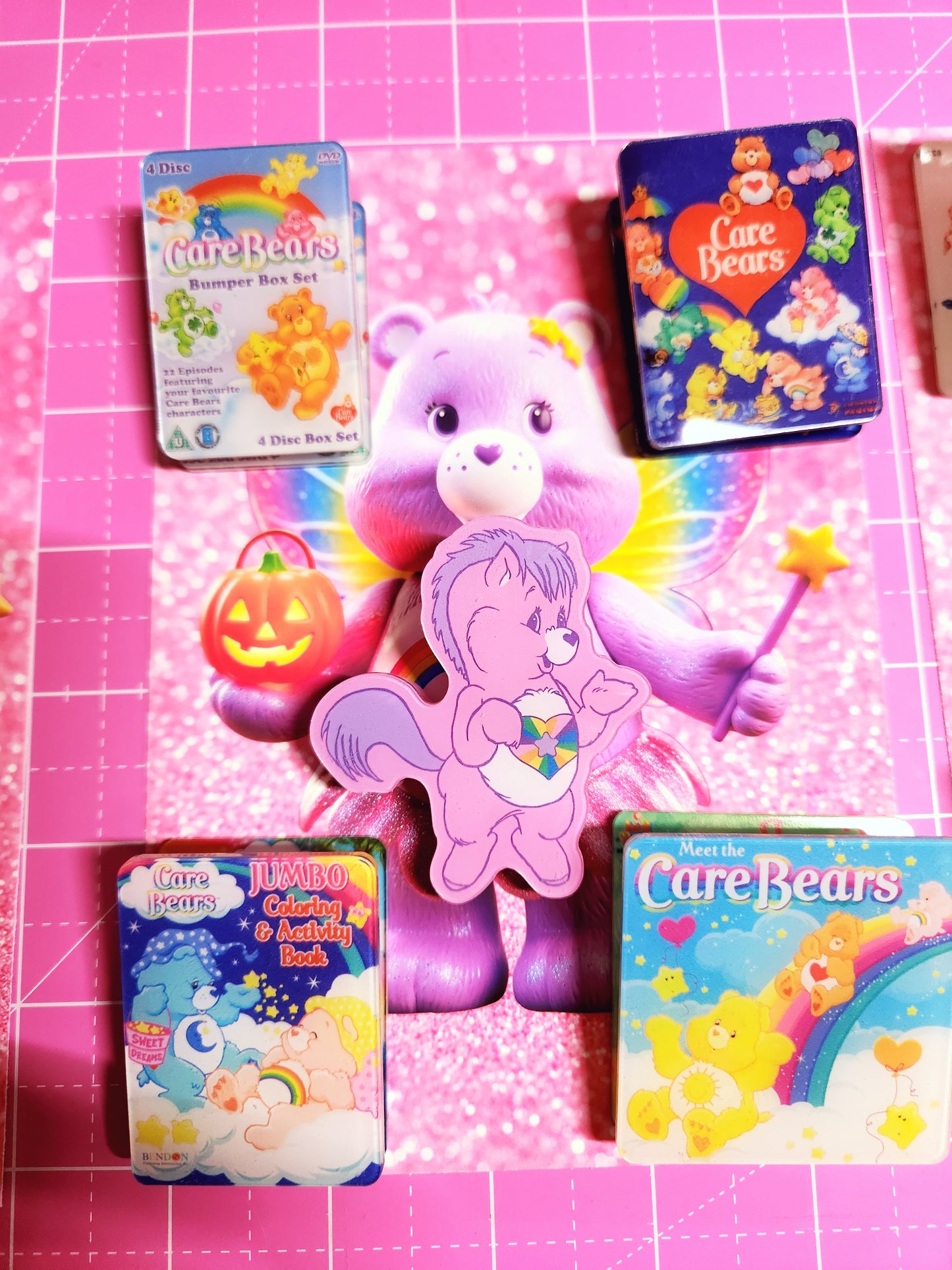 Collection of Care Bears toys and items on a pink grid background
