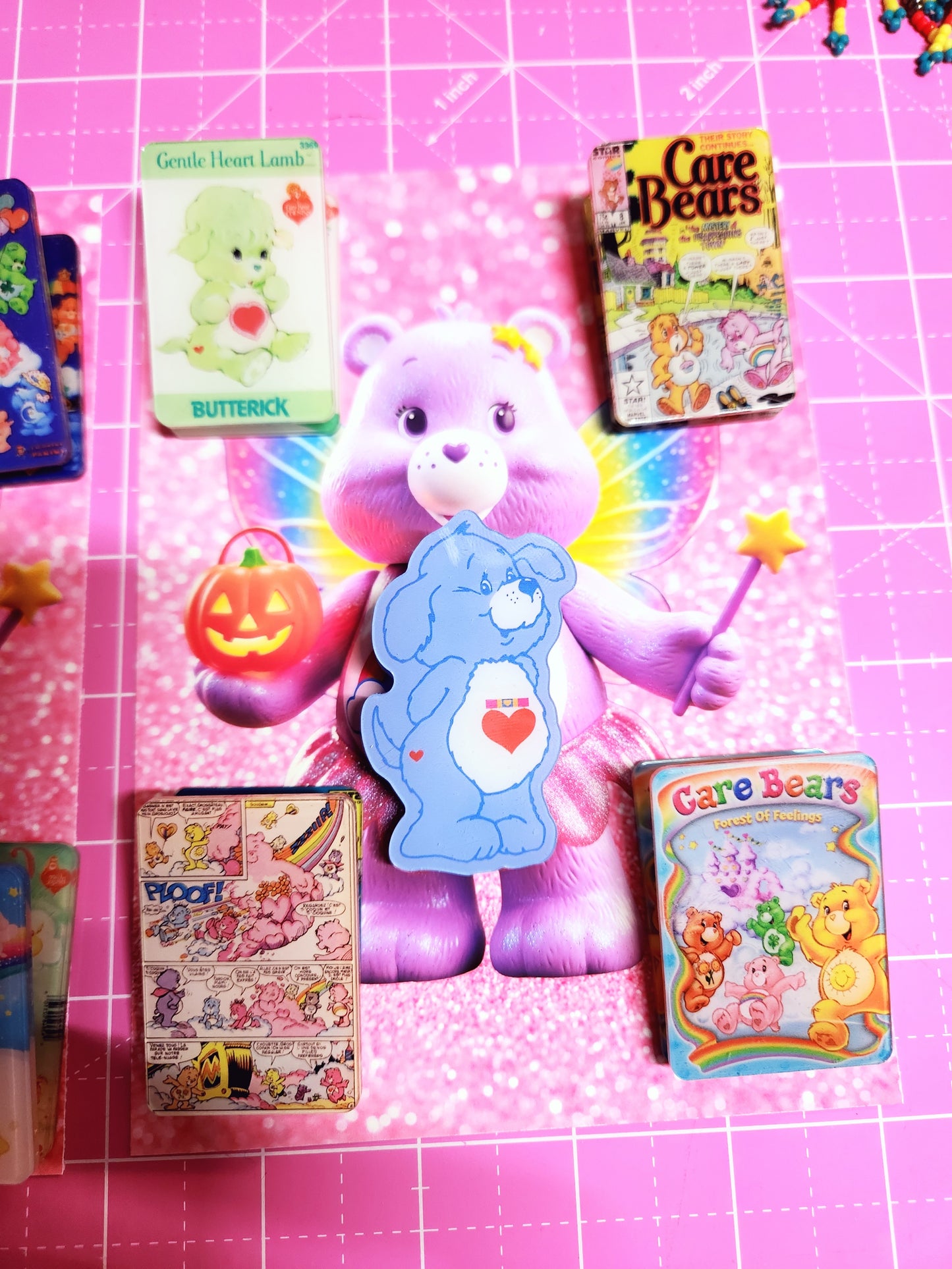 Collection of Care Bears toys and books on a pink grid background