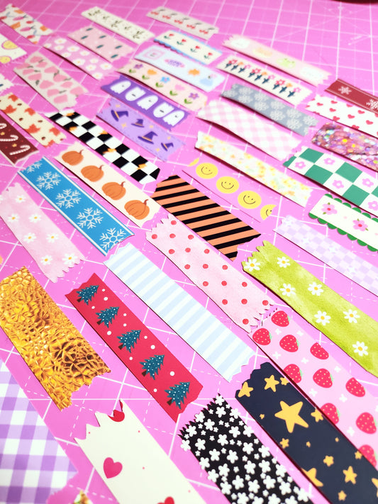Collection of colorful washi tape rolls on a pink grid background