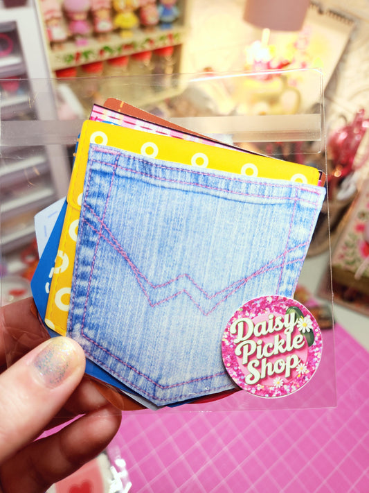 Hand holding a small denim notebook with colorful stickers in a store setting