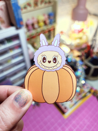 Cartoon character sticker on a pumpkin held by a hand with colorful background