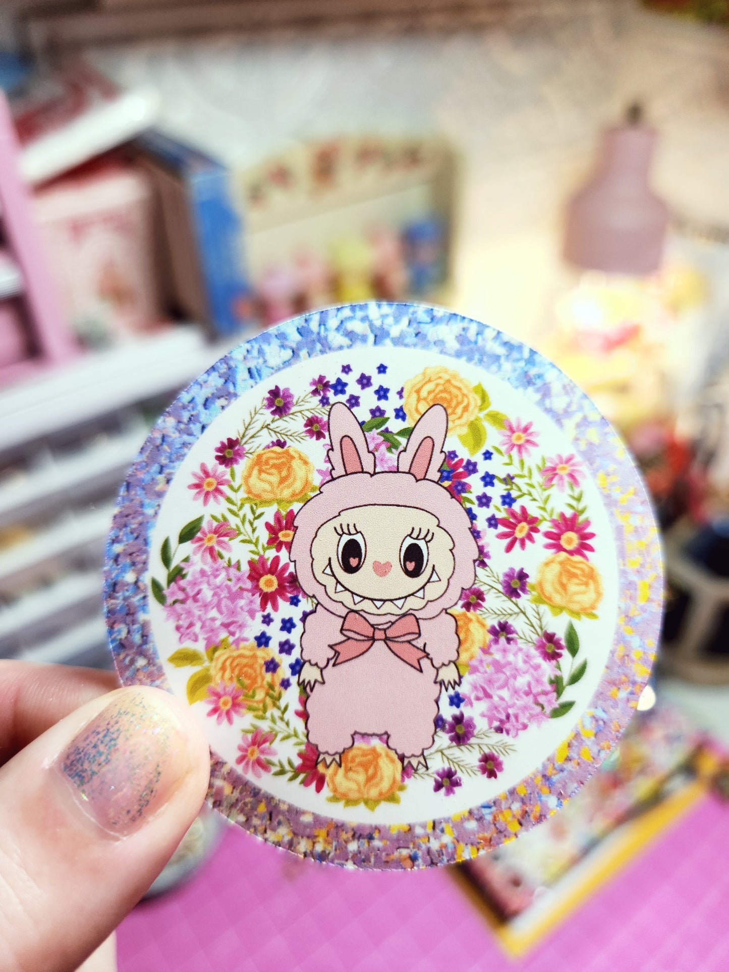 Circular sticker with cartoon character and flowers held by a hand against a blurred background