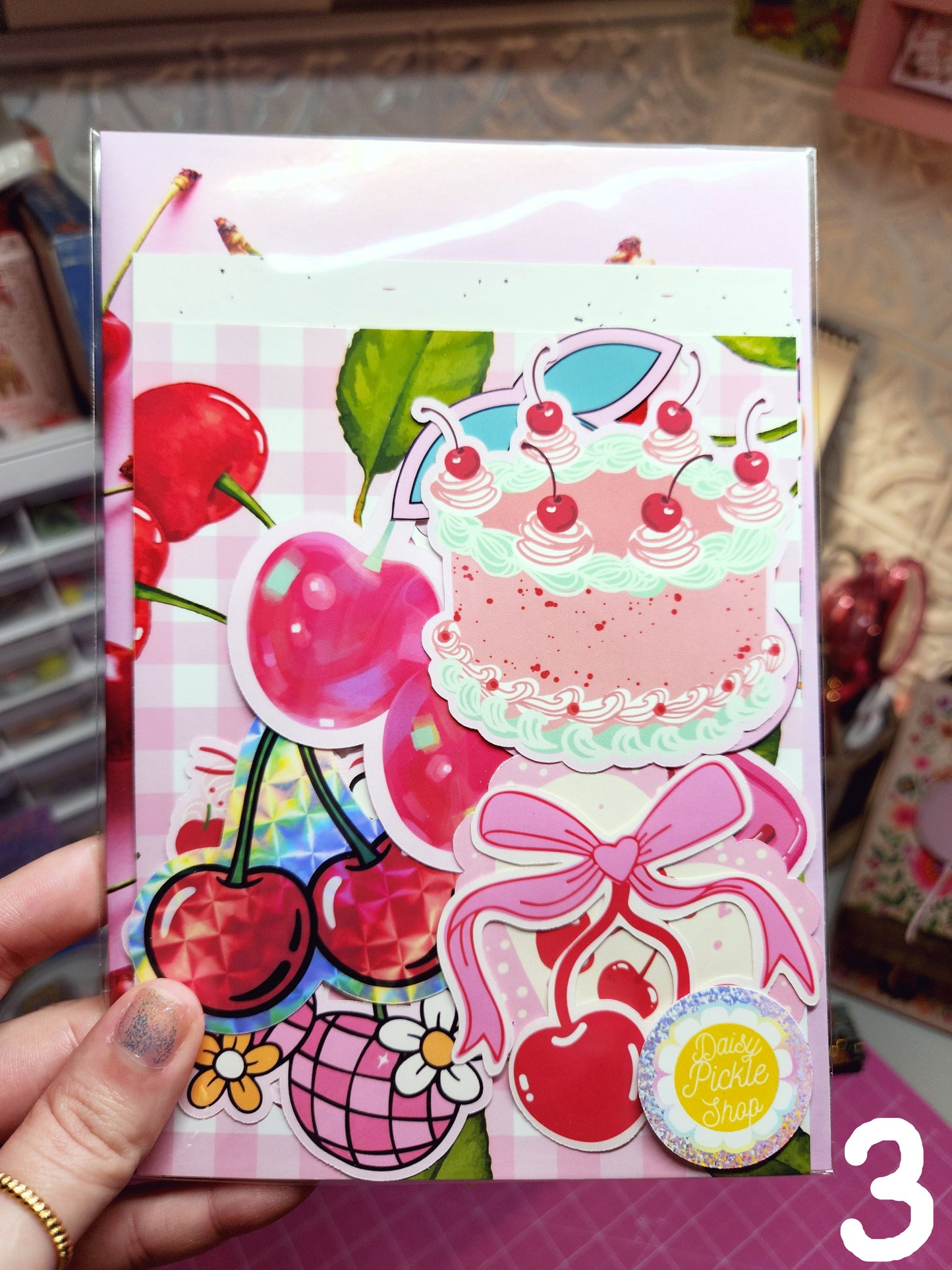 Colorful decorative paper with cherries and bows held by a hand on a pink background