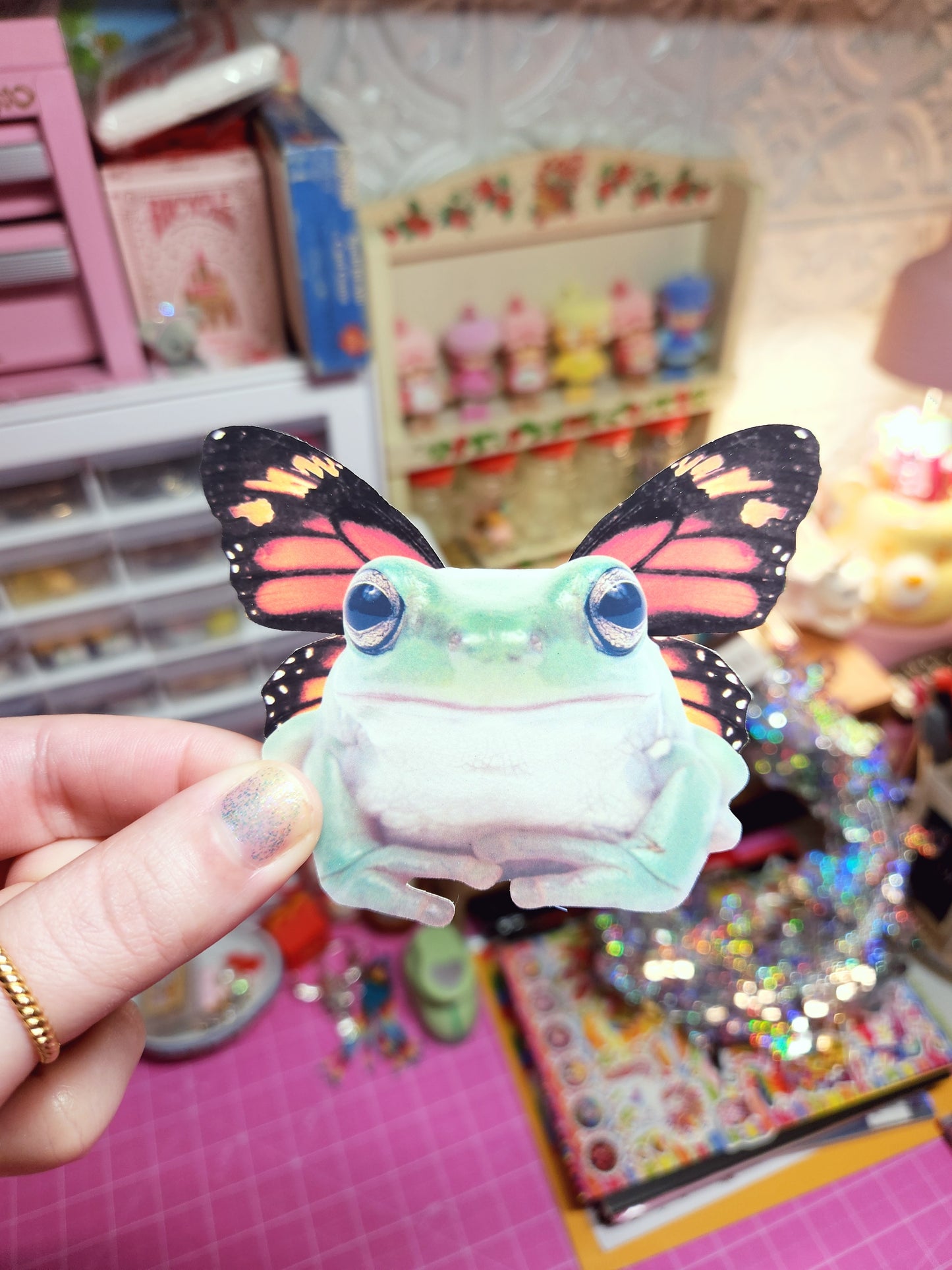 Hand holding a colorful butterfly-shaped ice cream cone against a vibrant, cluttered background.