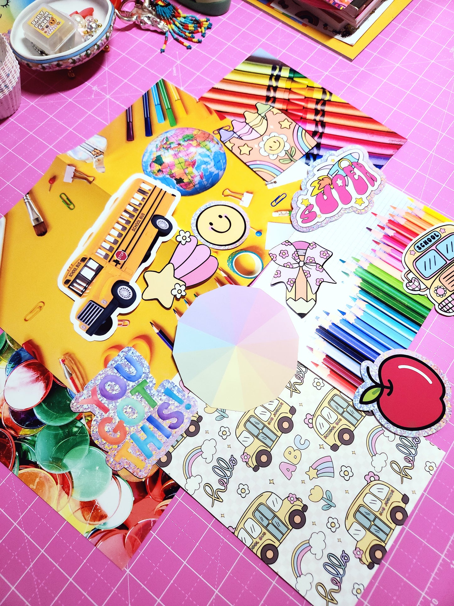 Colorful stationery items including crayons, stickers, and a coloring book on a pink grid background.