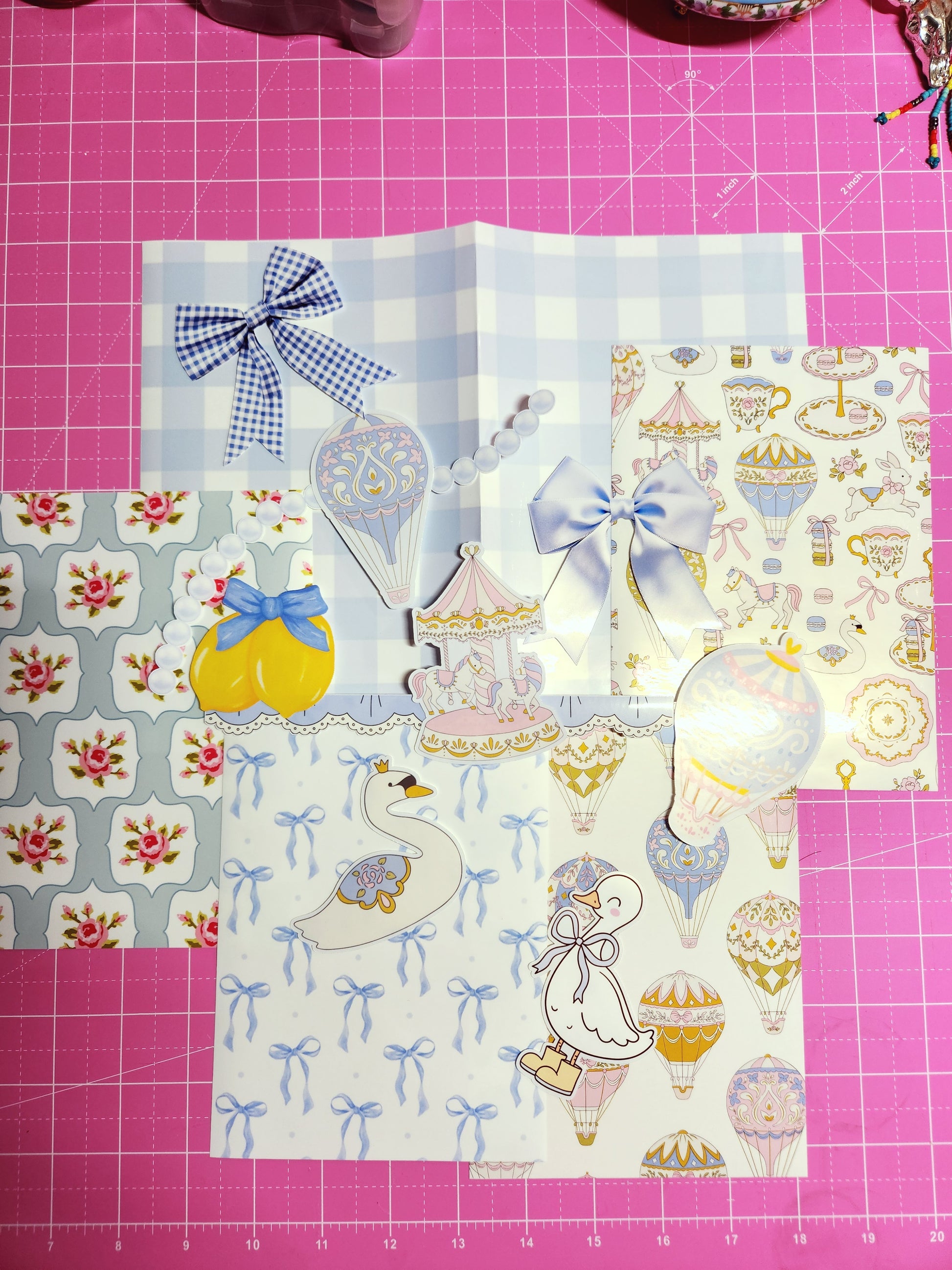 Decorative paper sheets with cartoon designs on a pink cutting mat.