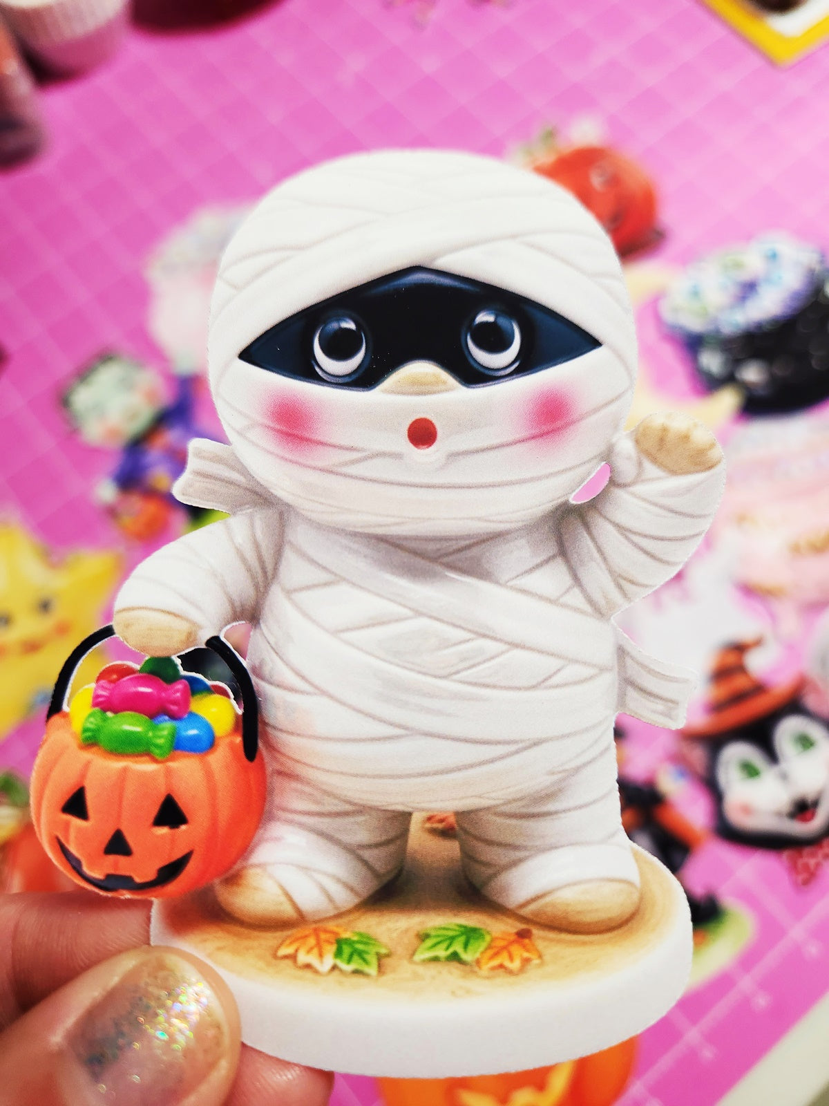 Toy figure of a mummy with a pumpkin bucket on a colorful Halloween-themed background