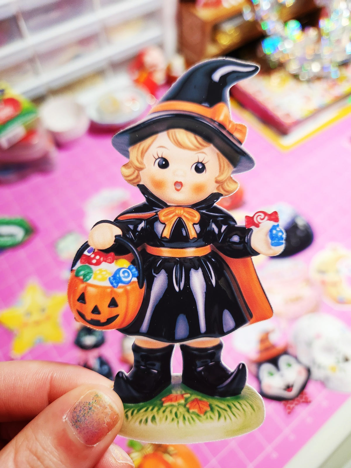 Halloween-themed figurine of a child in a witch costume holding a pumpkin bucket.