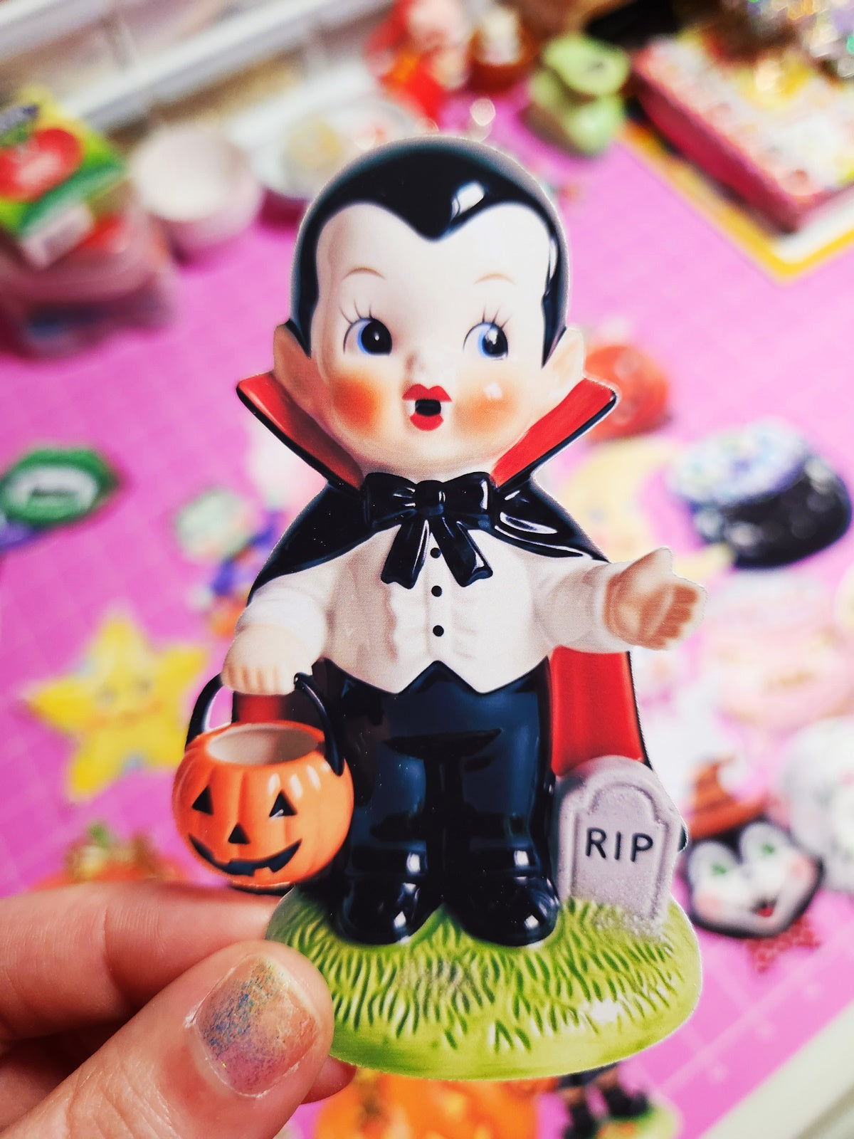 Vampire figurine with a pumpkin and gravestone on a colorful Halloween-themed background