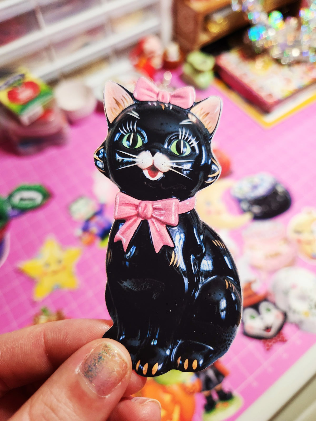 Black cat figurine with a pink bow held by a hand on a colorful background