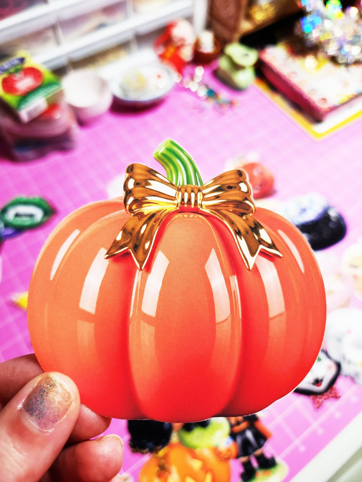 Orange pumpkin-shaped container with a gold bow held by a hand on a colorful background