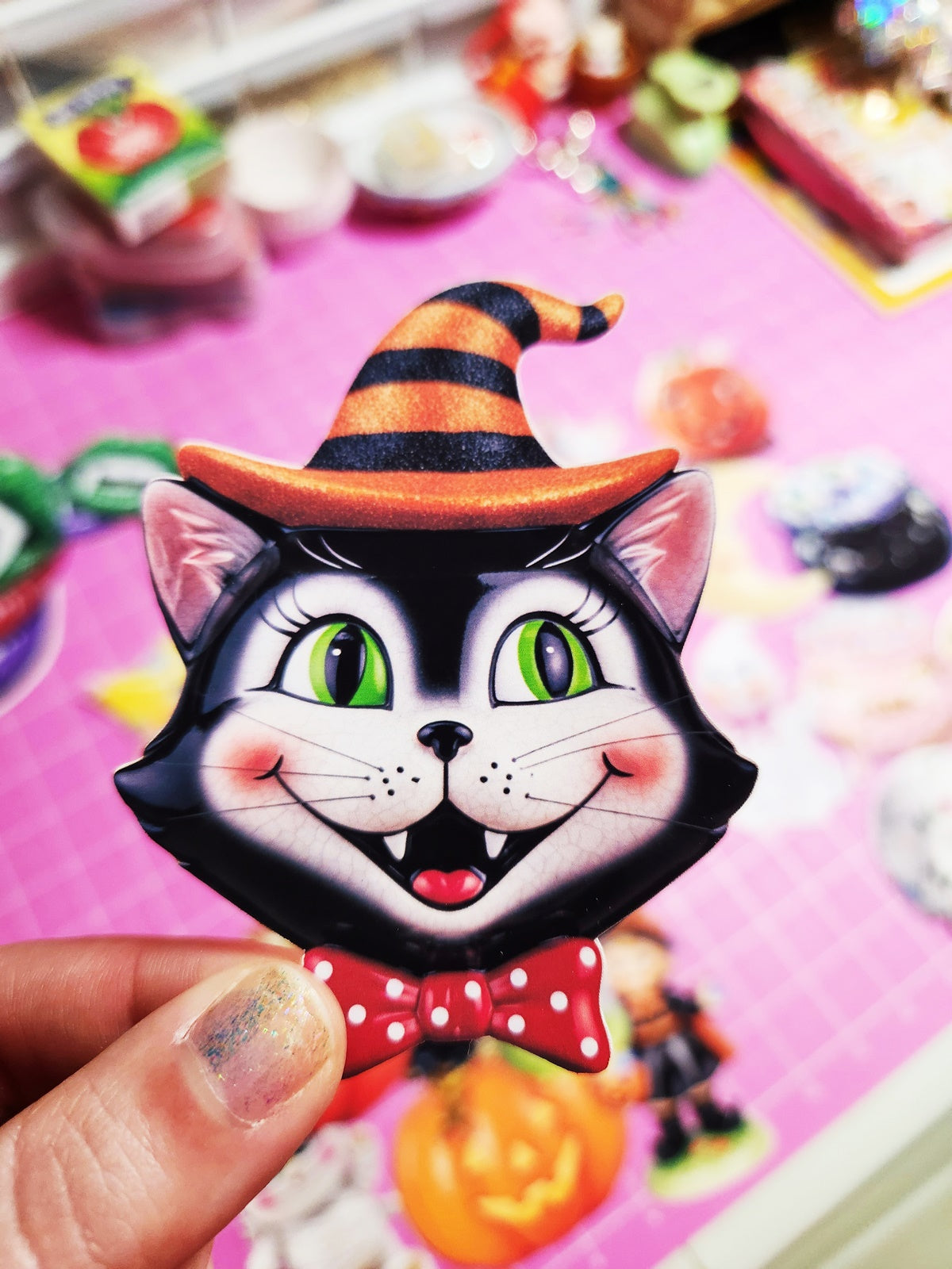 Halloween-themed cat pin with a witch hat held in front of a colorful background.