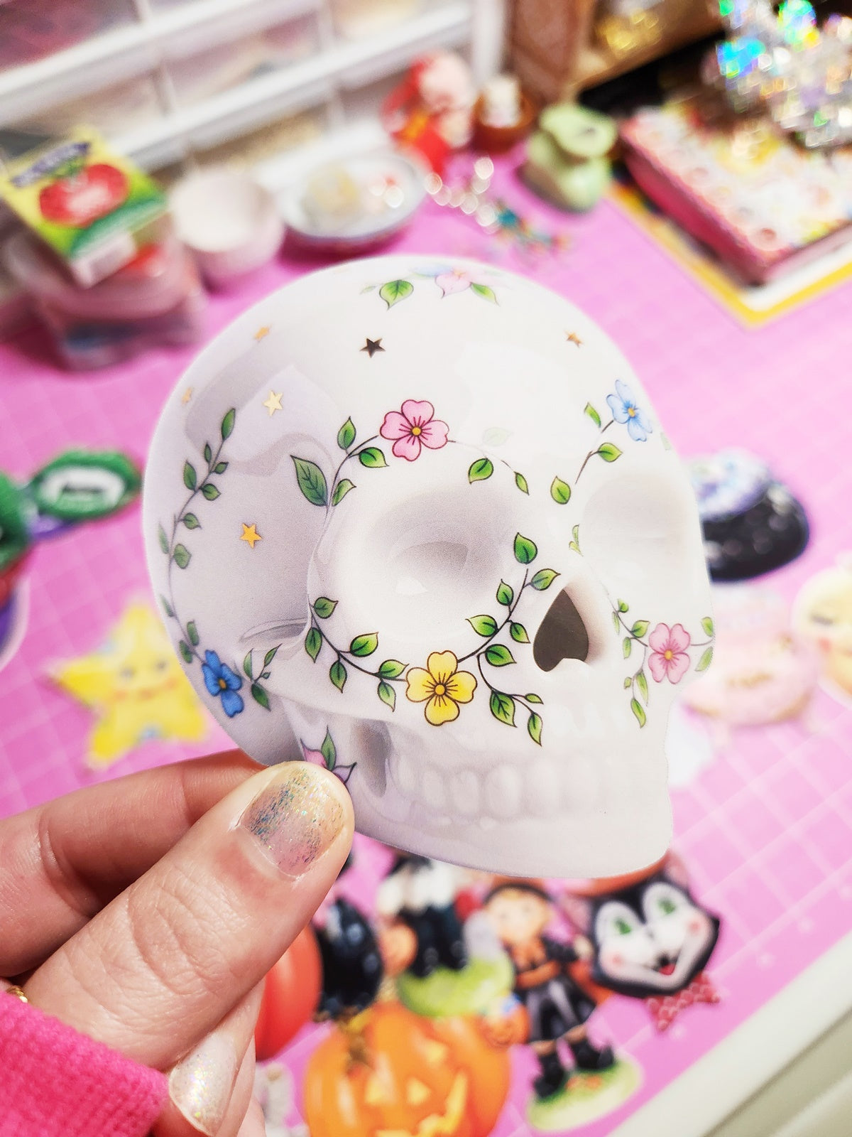 Decorative skull with floral designs held by a hand on a colorful background
