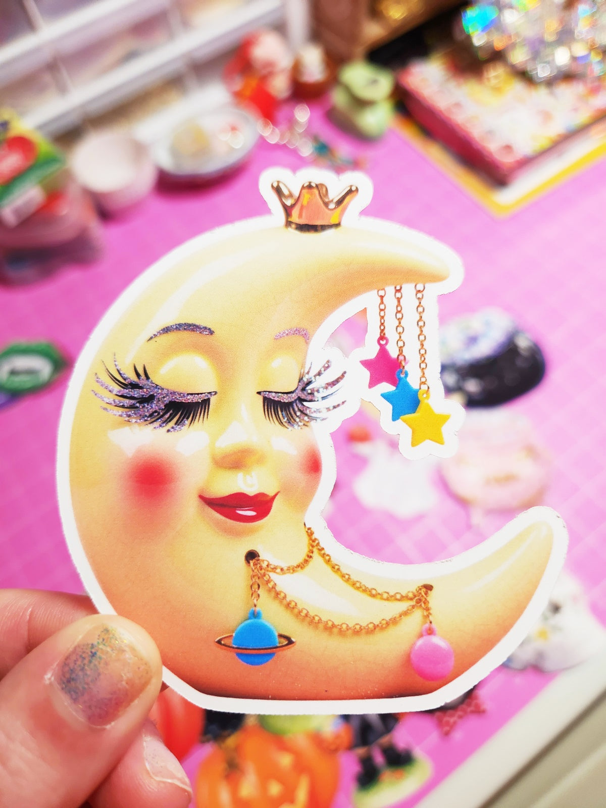 Decorative item with a face on a crescent moon, featuring stars and a crown, held by a hand.