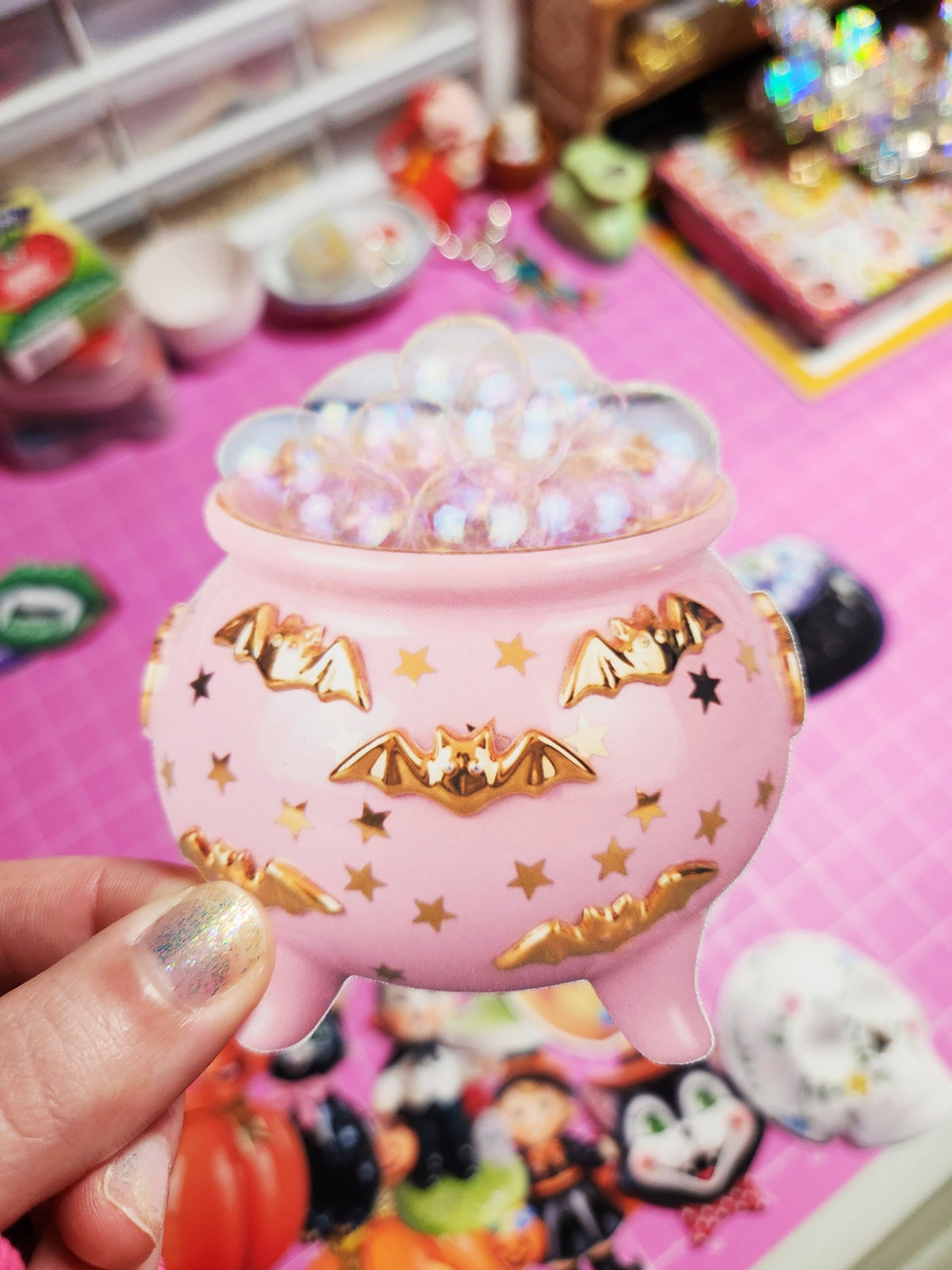 Pink decorative container with gold accents held by a hand against a colorful background.