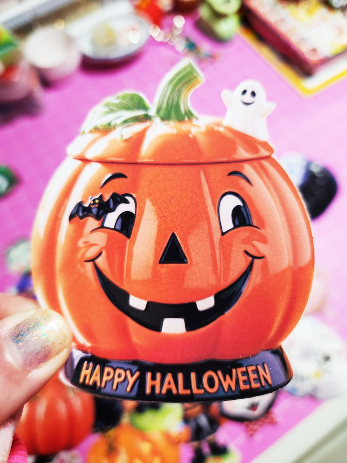 Pumpkin-shaped container with a face and 'Happy Halloween' text, held in front of a festive background.