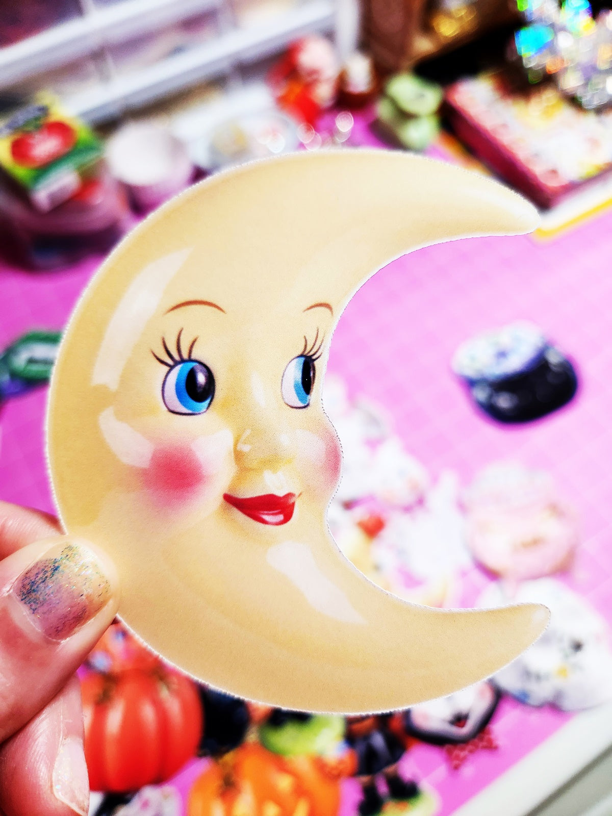 Cartoon moon with face design held by a hand against a colorful background