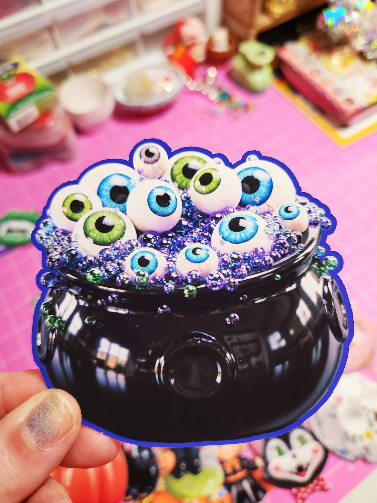 Decorative item with multiple eyes and colorful embellishments on a pink surface.